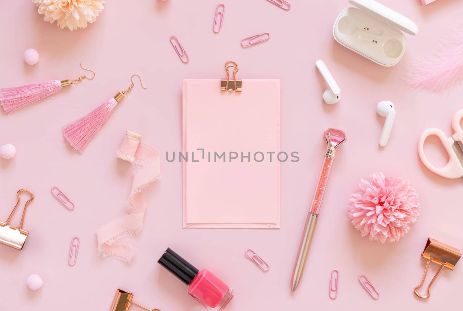 Paper with a clip and Pink school accessories on pastel pink, top view, textbook mockup. Girly workplace with scissors, pencils, pen, paperclips, earrings and watch. Back to school concept