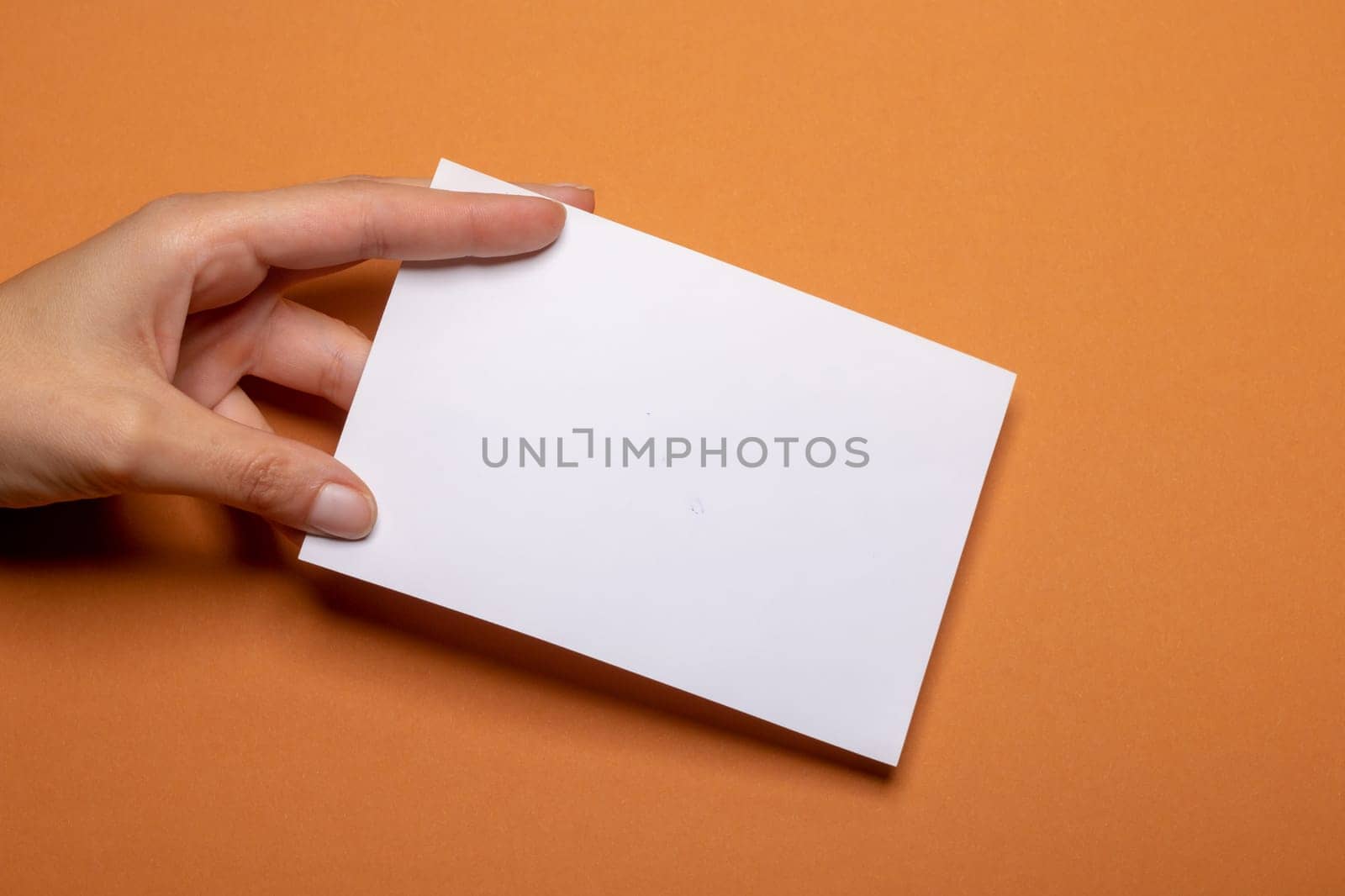female hand holds a blank piece of paper with copy space in front of a tangerine colored background cardboard