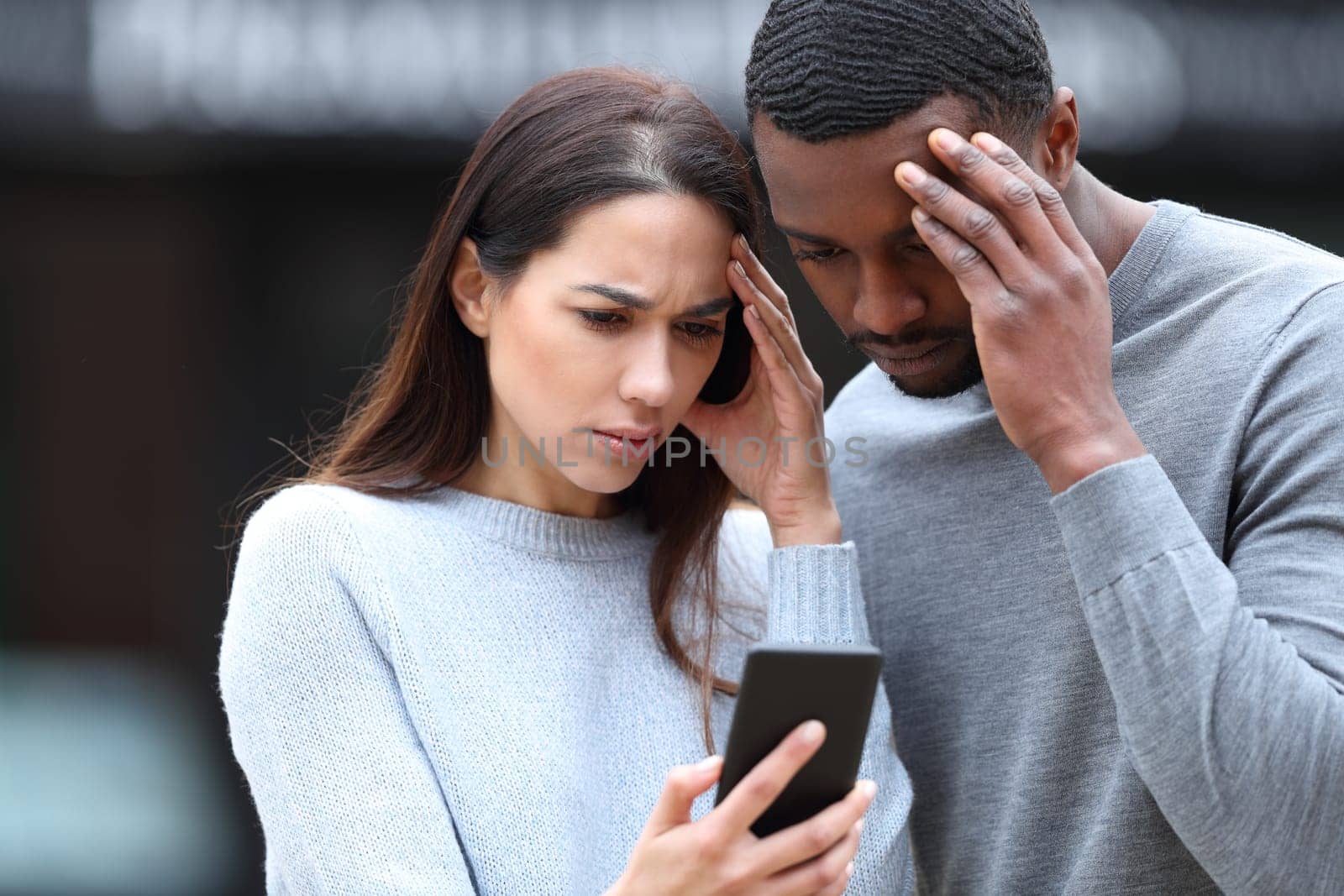 Worried interracial couple checking phone in the street