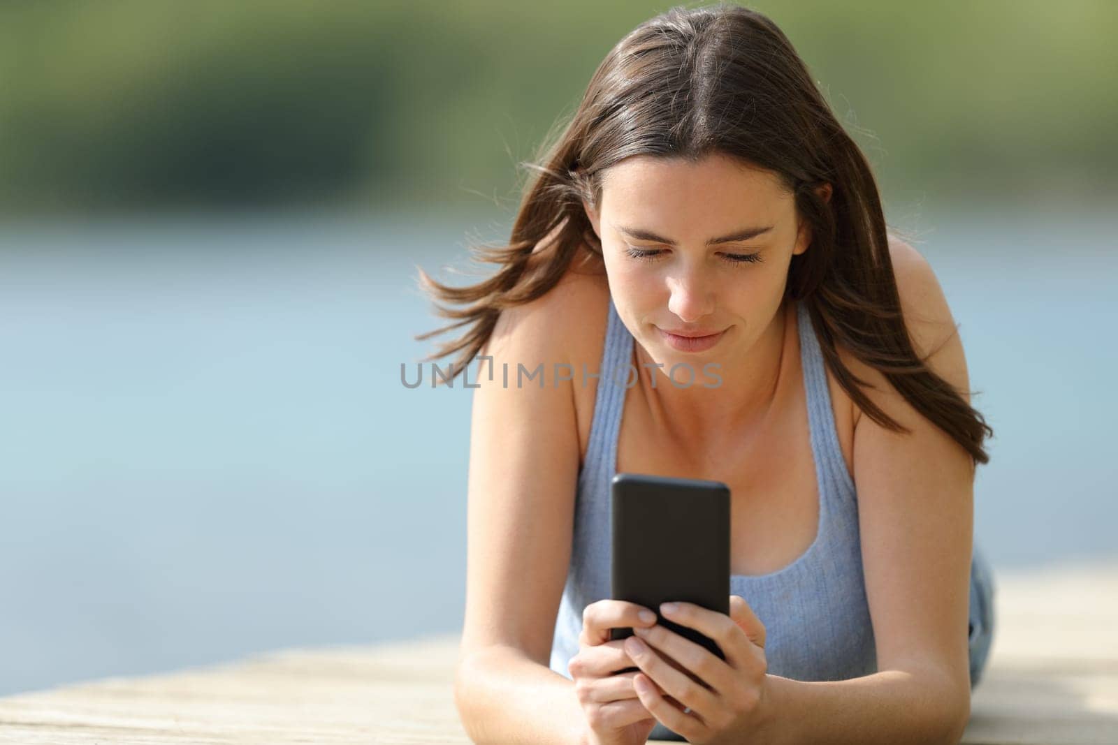 Woman using mobile phone lying on pier