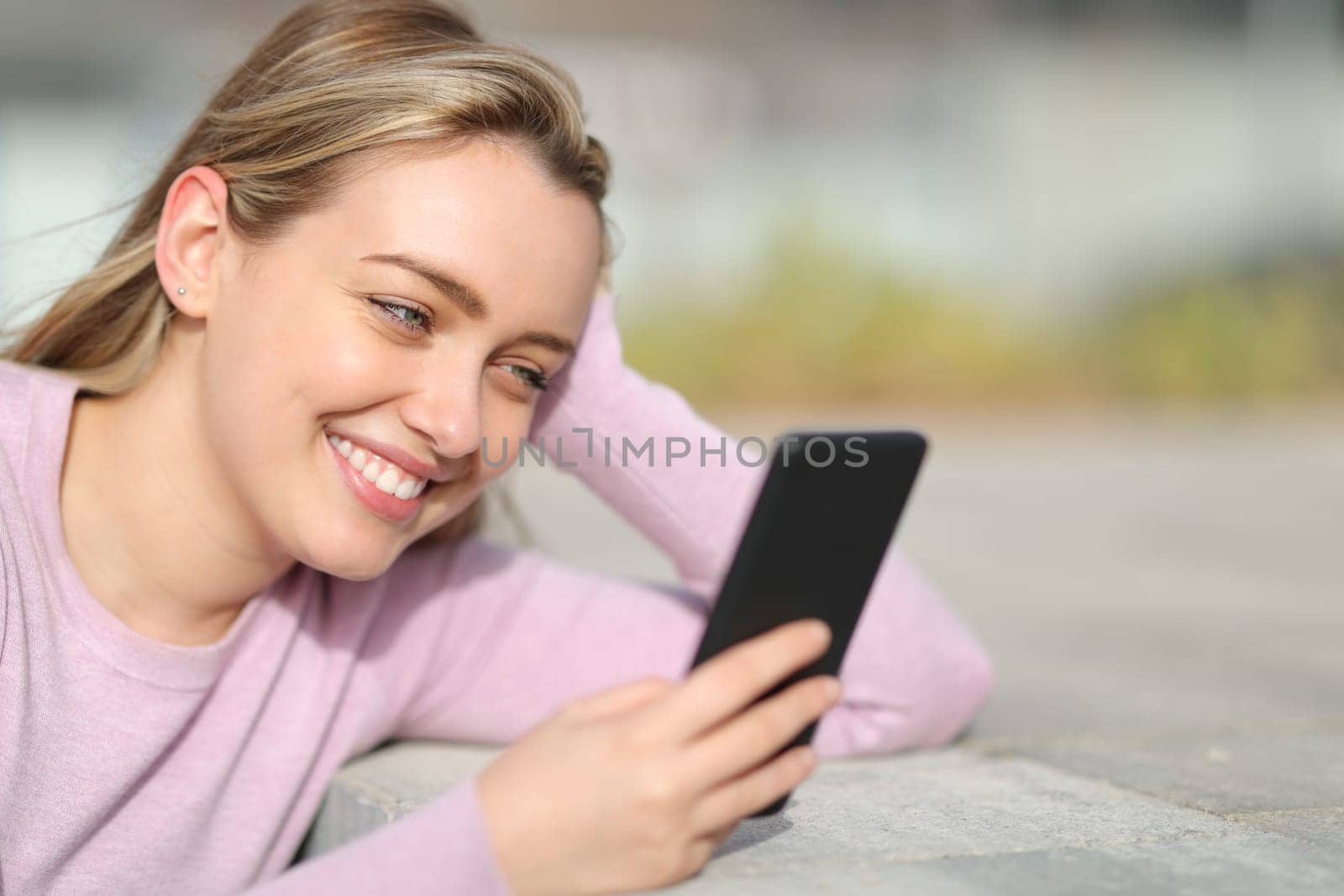 Happy teen smiling using phone in the street