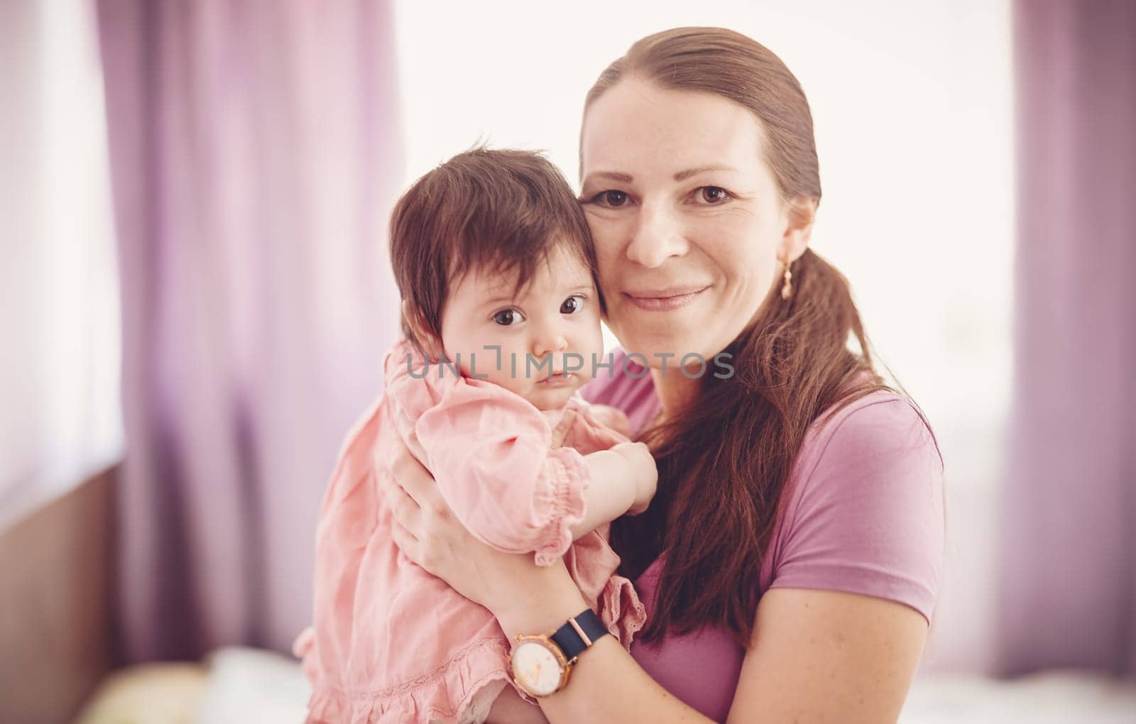 Mother holding in her hands cute daughter indoors. Concept of motherhood.