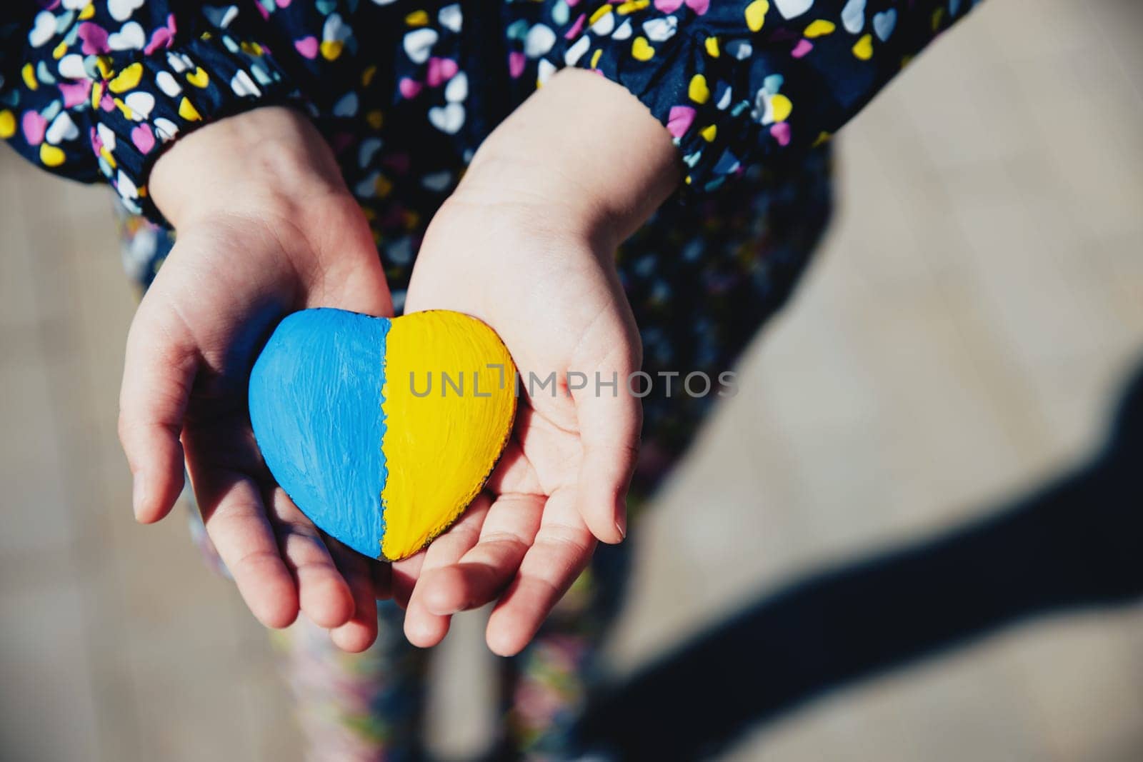 Small little kid hold heart shaped stone with Ukraine blue-yellow national flag or anthem. Girl love native country. Child stand for Ukrainians. Stop war, agression, invation. People agains the war.