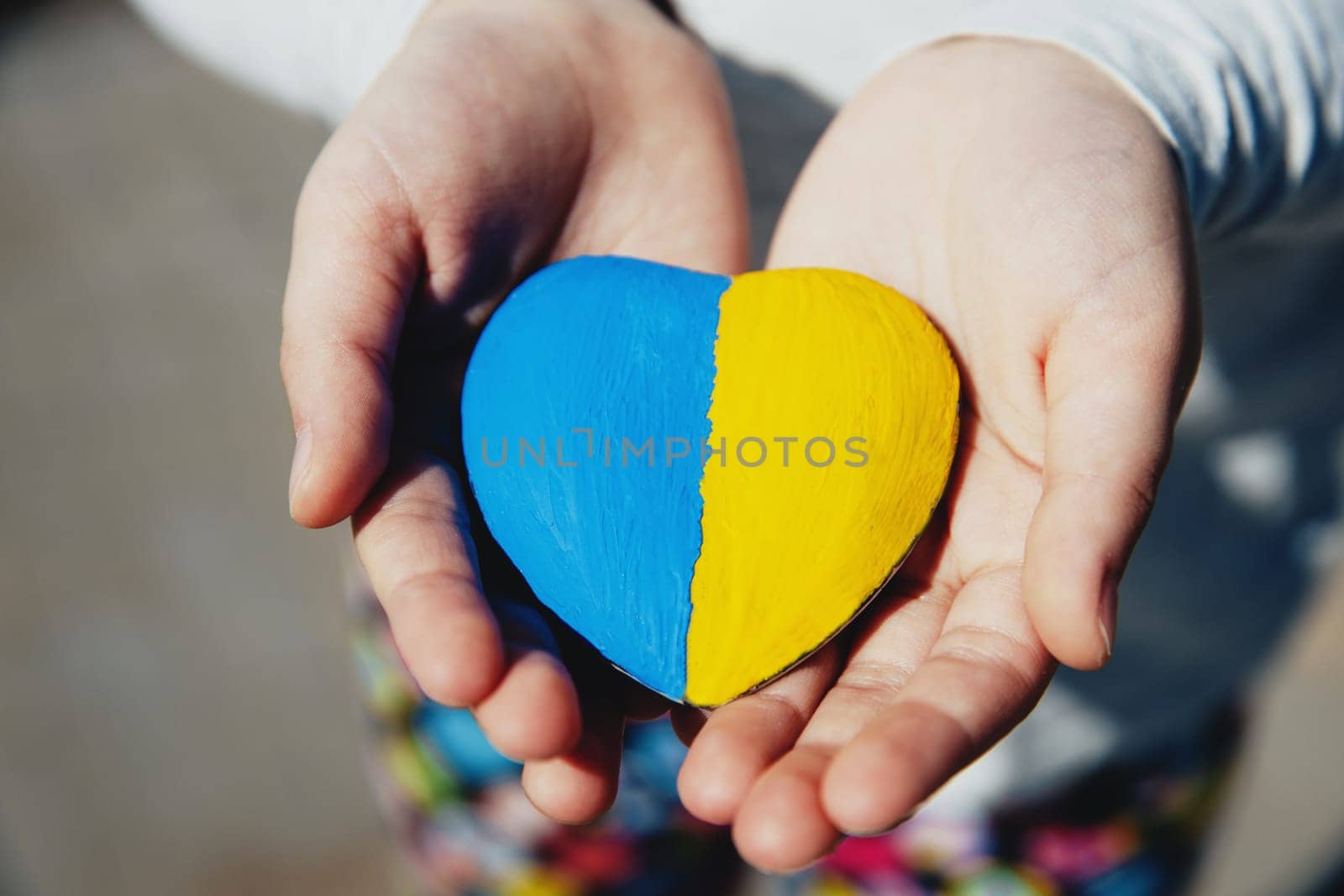 Small little kid hold heart shaped stone with Ukraine blue-yellow national flag or anthem. Girl love native country. Child stand for Ukrainians. Stop war, agression, invation. People agains the war.
