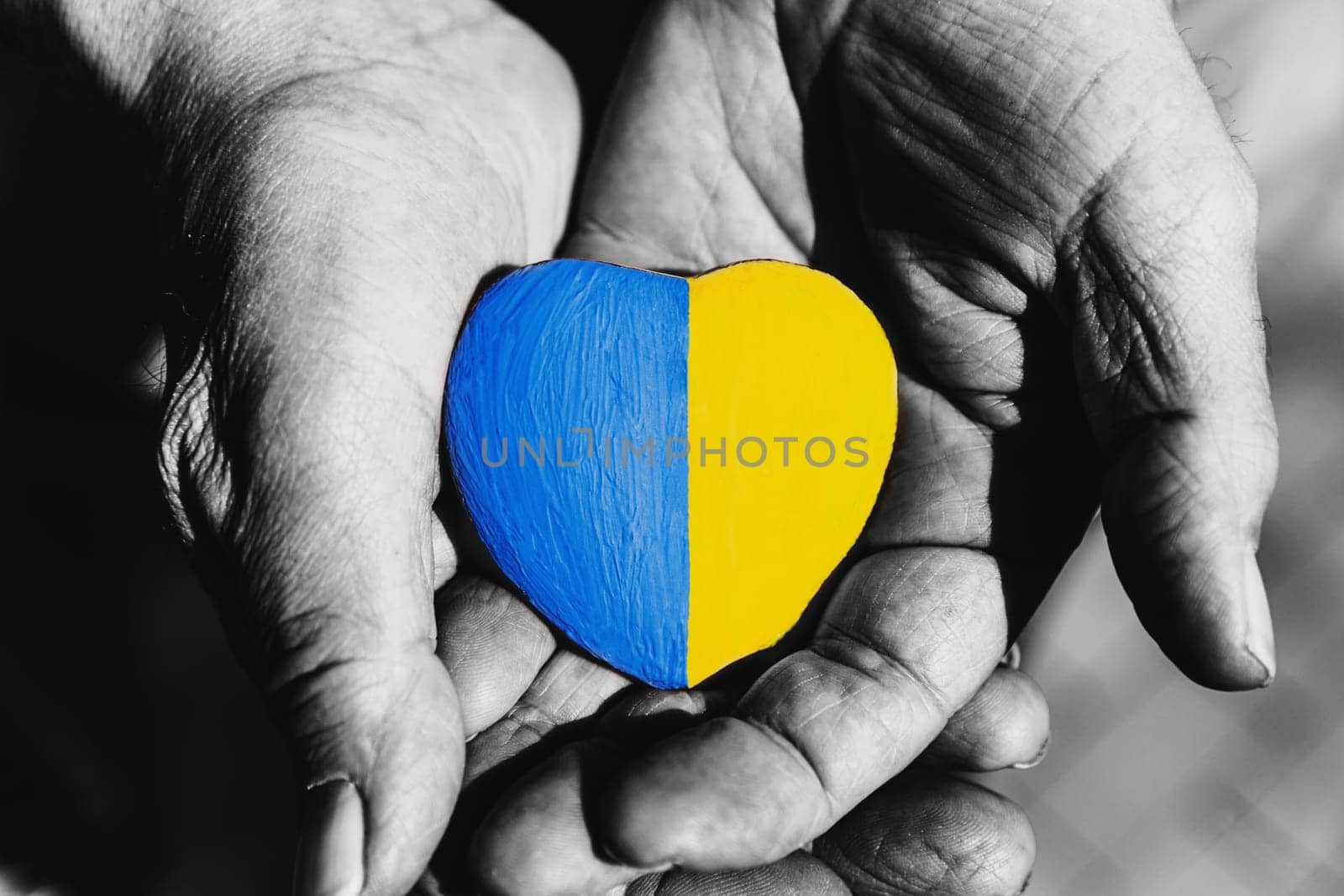 Senior man or soldier hands holding heart shape stone painted with Ukraine national flag colors. Pray for Ukraine, stop the war, save Ukraine people and children. No invasion, occupation and terrorism