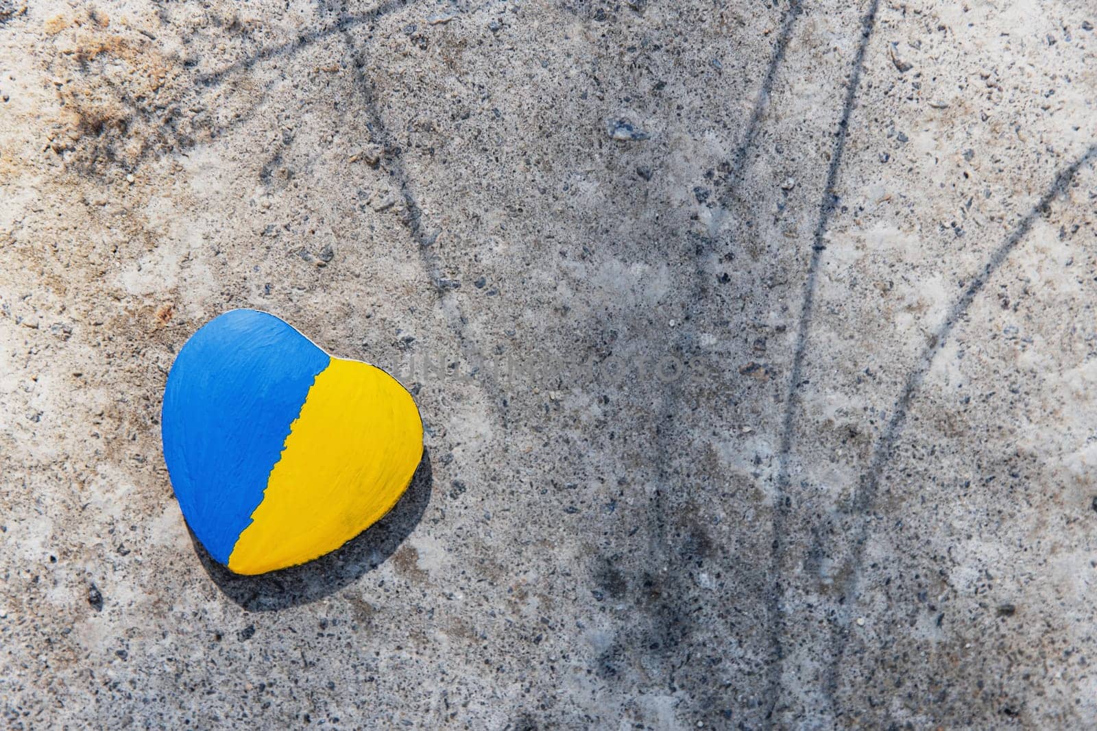 Stone in shape of a heart painted with the Ukrainian flag lies on the ground or concrete. No war. Stop the war, the genocide of Ukrainians. Flat lay with copy space. Save Ukraine people from invasion.