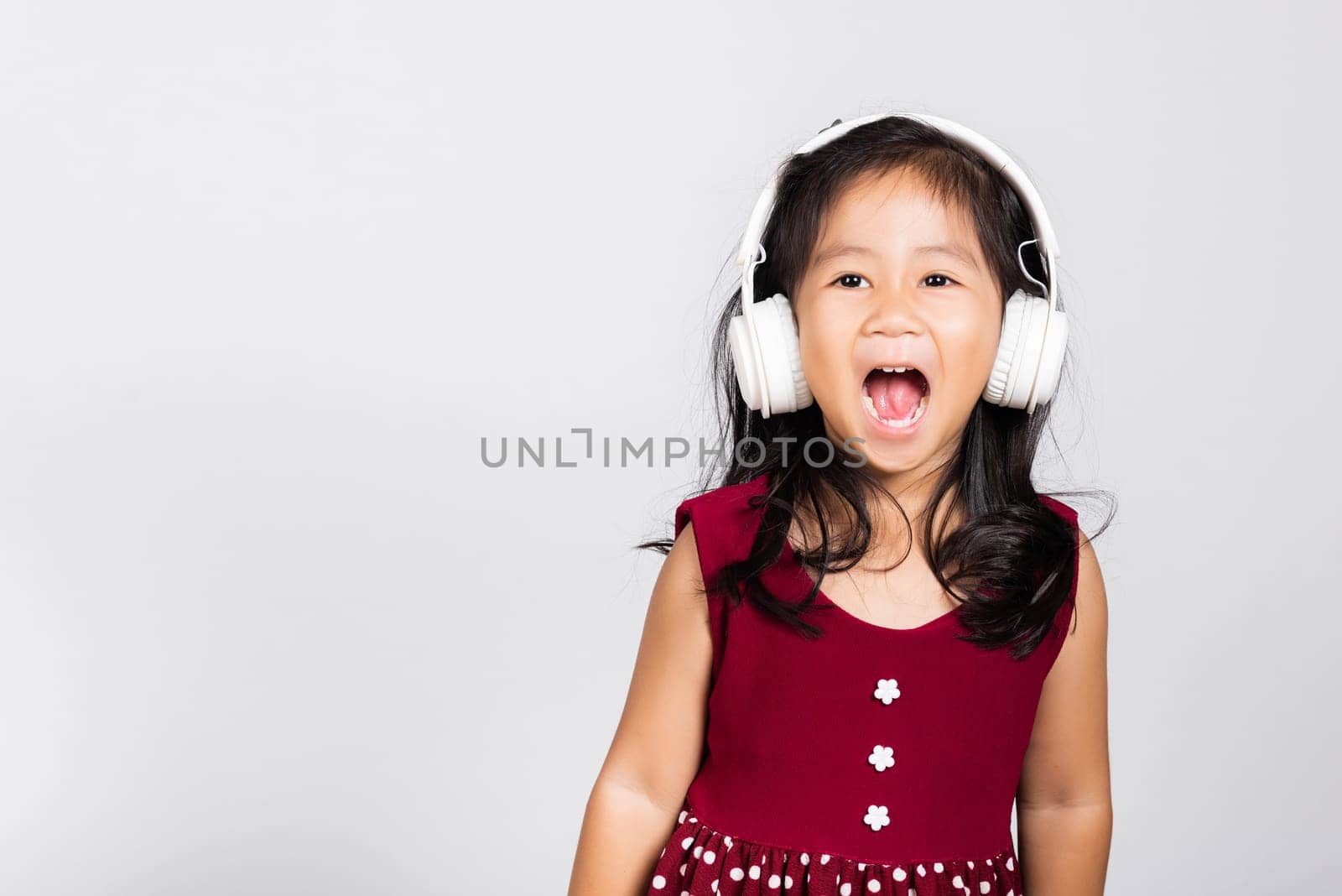 Little cute kid girl 3-4 years old listen music in wireless headphones in studio shot isolated on white background, happy Asian children smiling listening audio, entertainment lifestyle