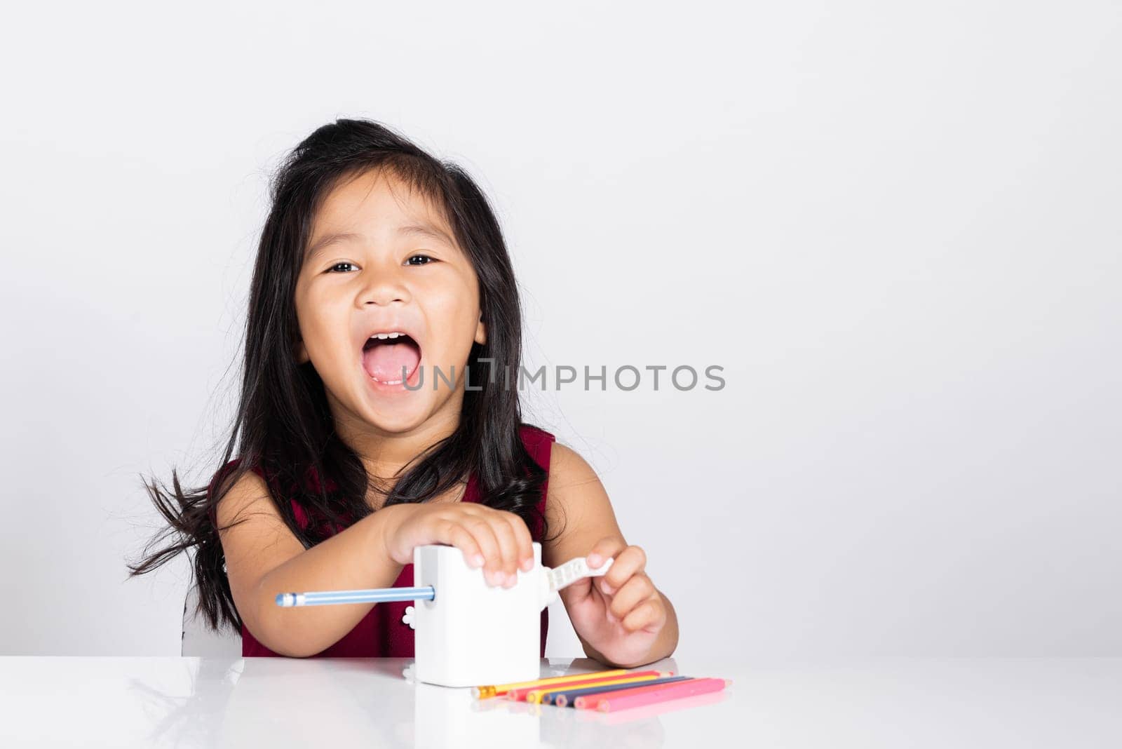 Little cute kid girl 3-4 years old smile using pencil sharpener while doing homework in studio shot isolated on white background, Asian children preschool sharpening color pencils, education concept