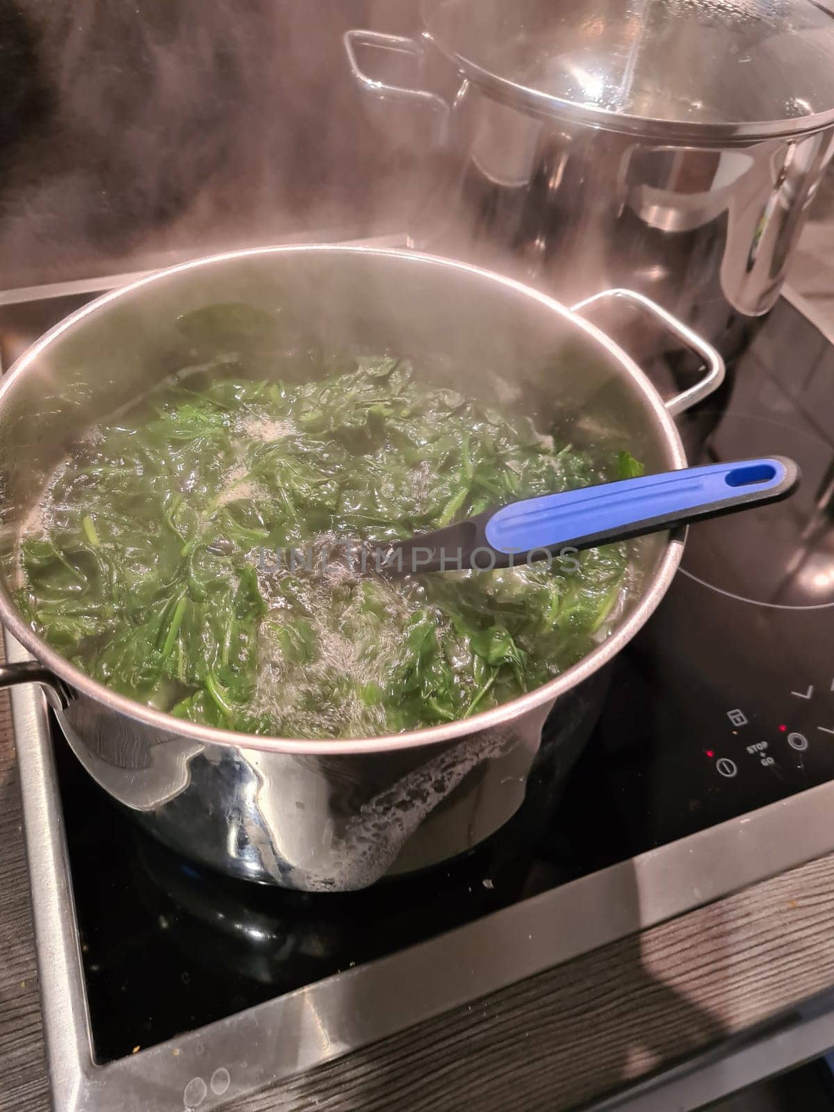 Spinach cooking preparation. Stewed spinach in black cooking pot with spoon on rustic background with ingredients and kitchen utensils . Top view. Home cuisine. Healthy food nutrition