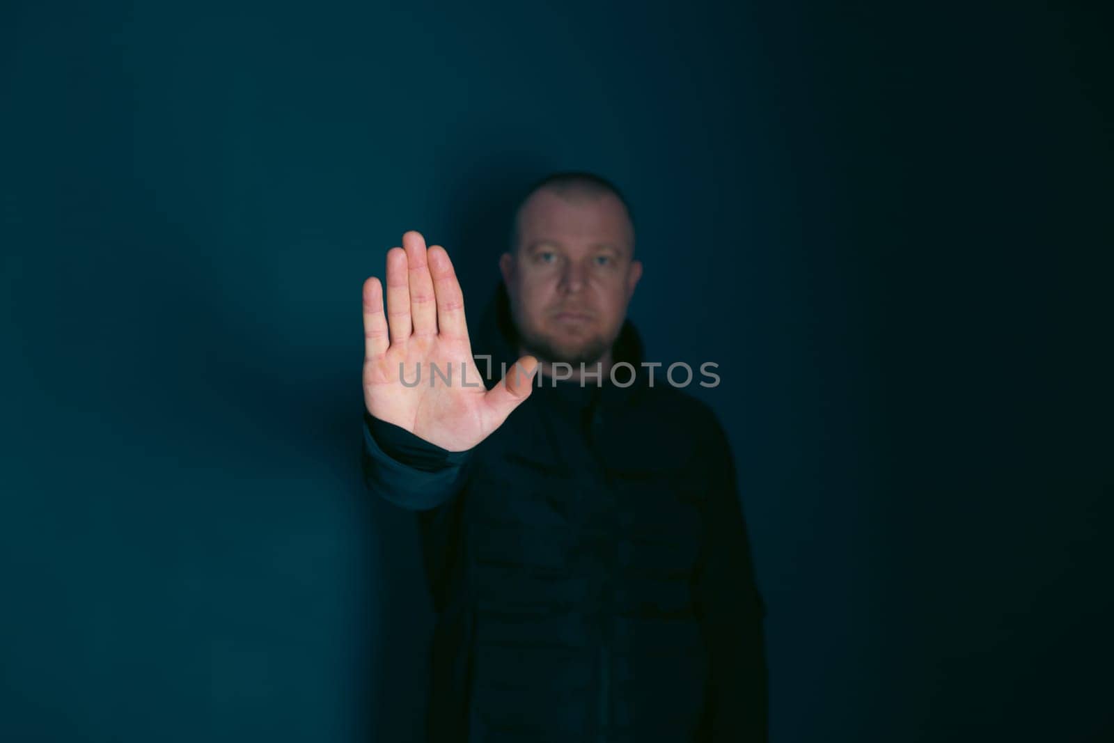 Sad, angry man showing stop sign on dark background. Low key photo.