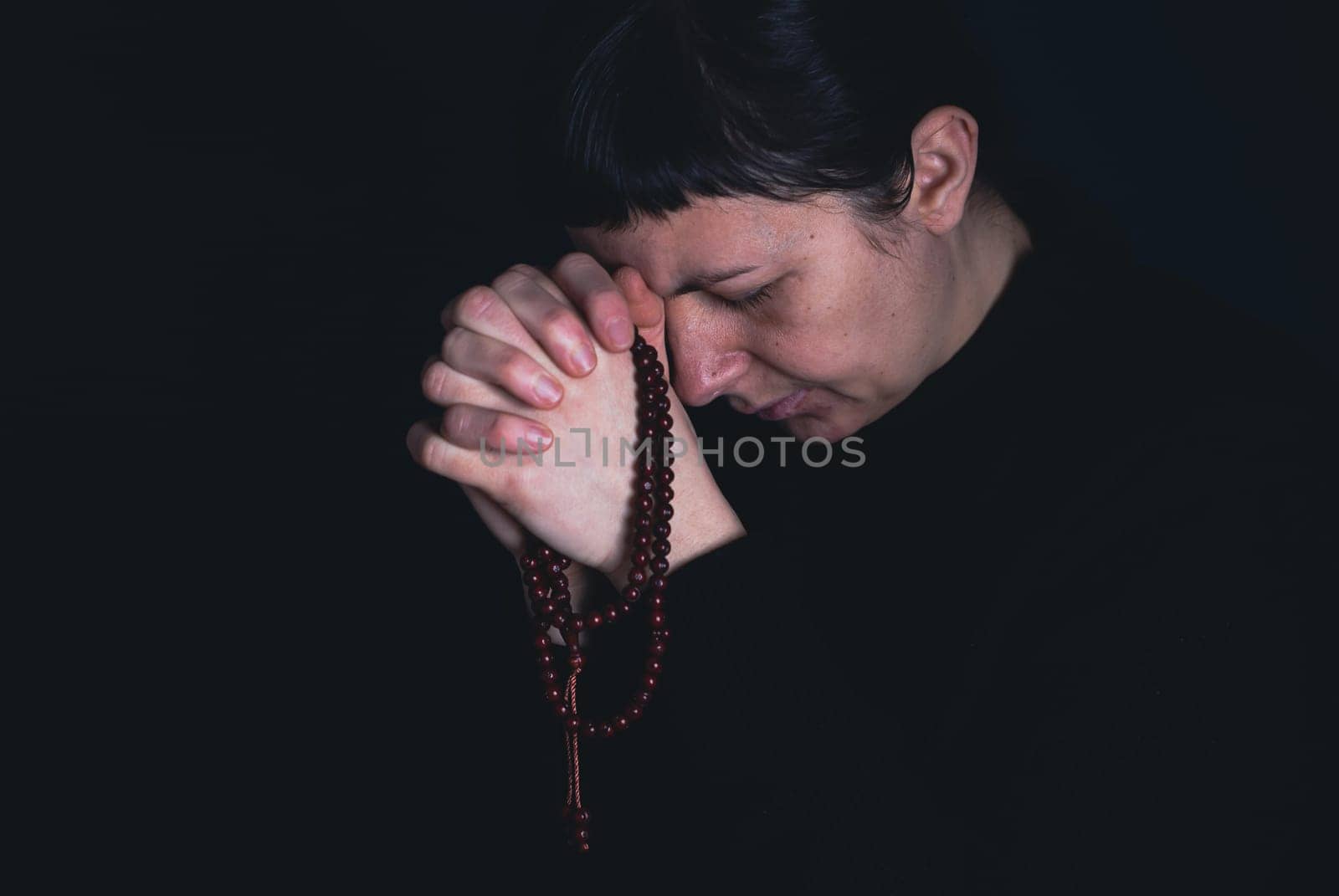 Religious young woman praying to God, on dark background.