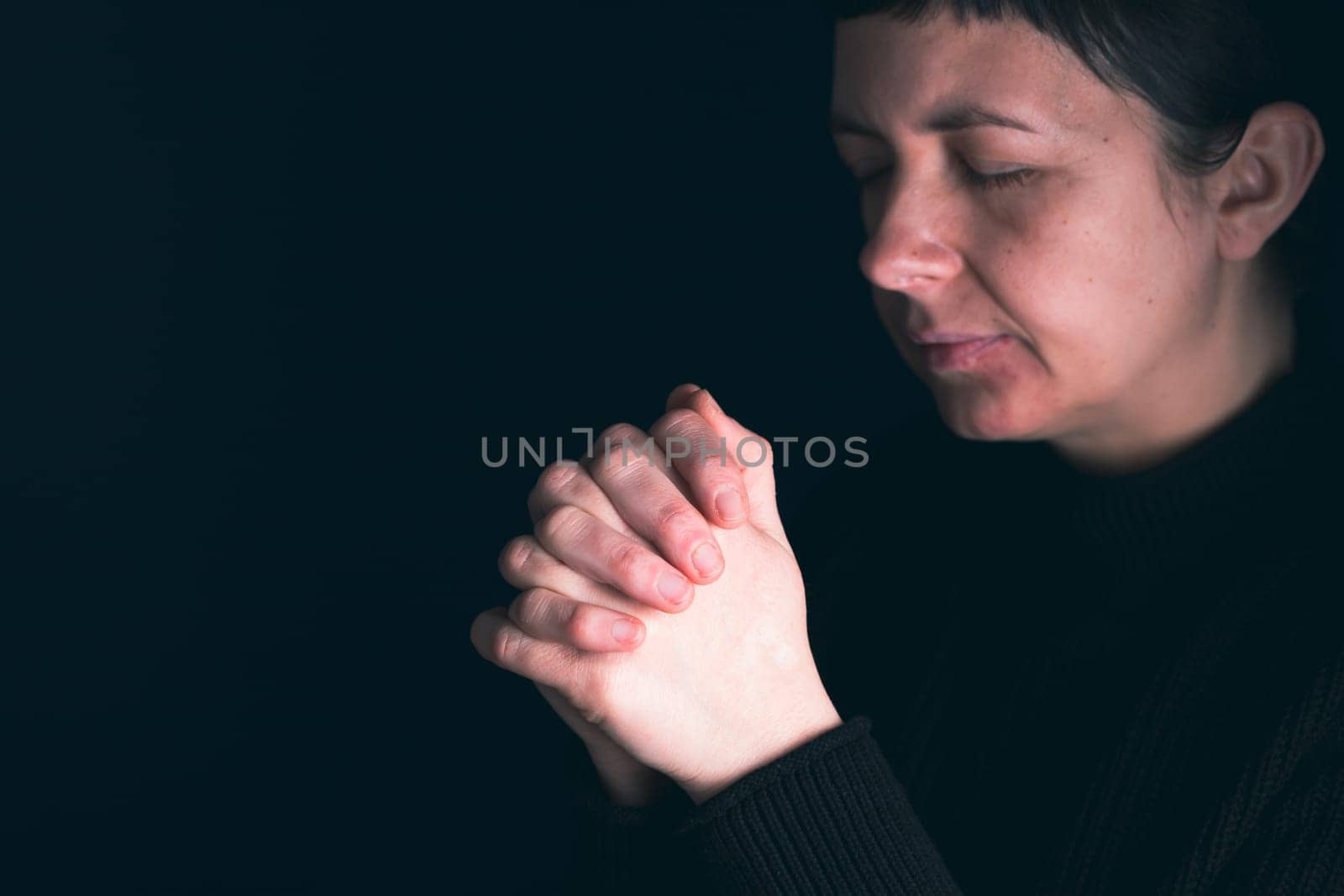 Religious young woman praying to God, on dark background.