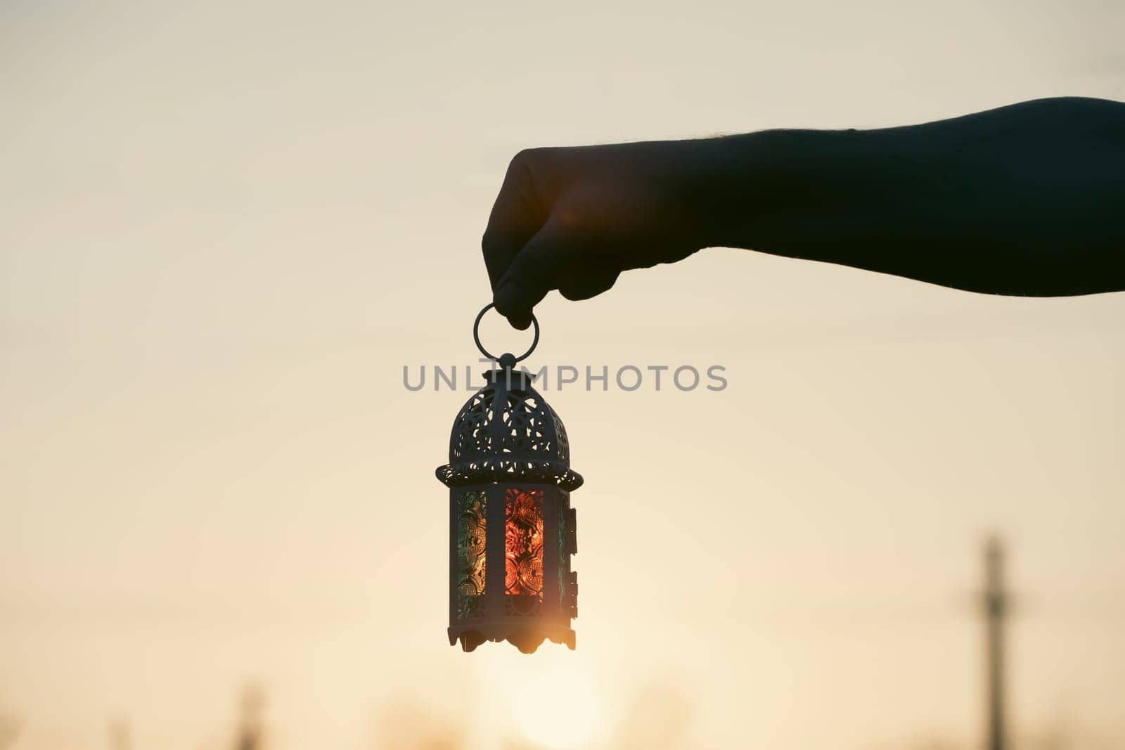 Ramadan Kareem background. Hand holding ornamental Arabic lantern in the sunset