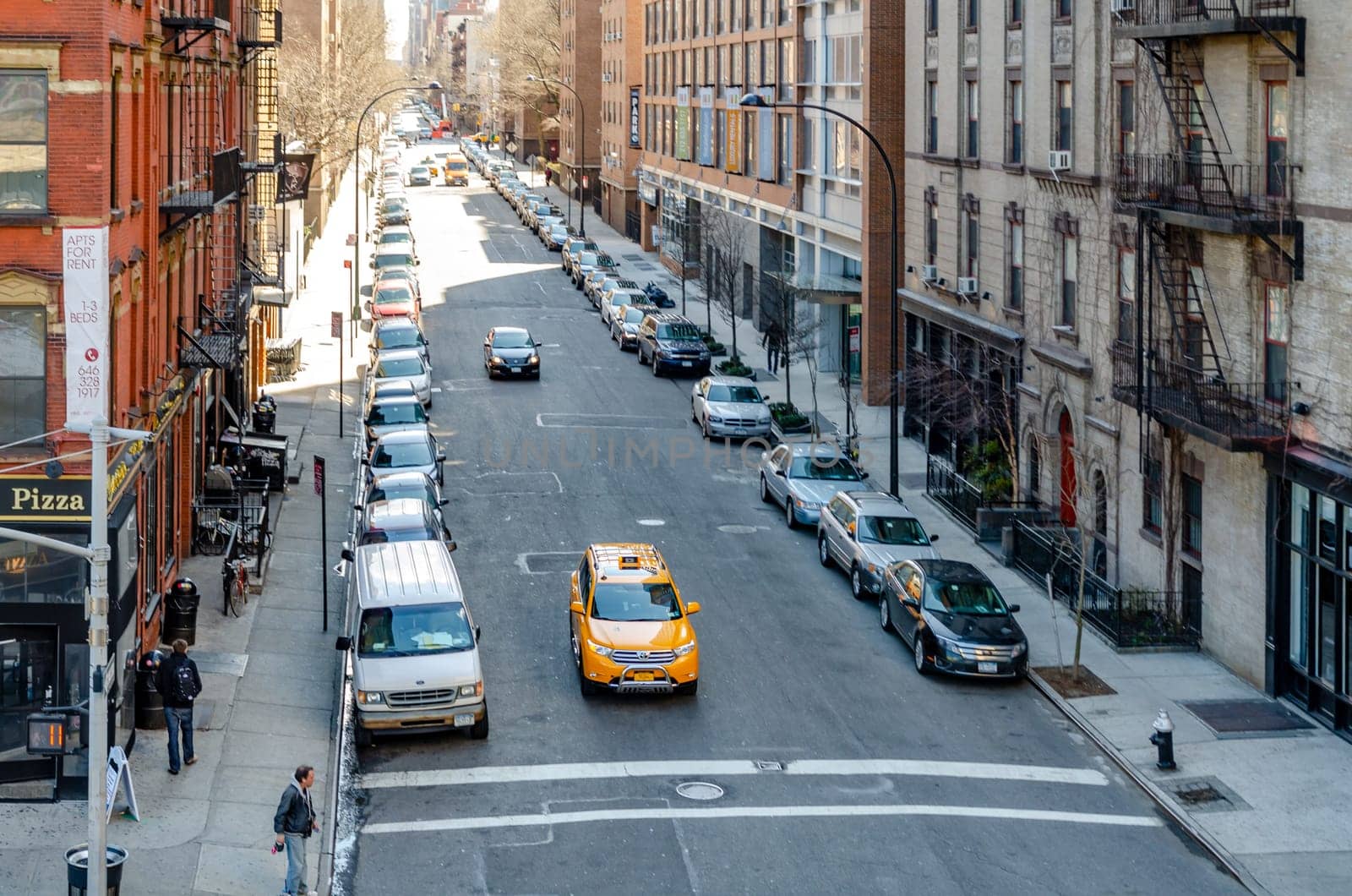 City street in Chelsea with yellow taxi cab in the front, people walking on the sidewalk, aerial view from the High Line Rooftop Park, New York City during sunny winter day, horizontal