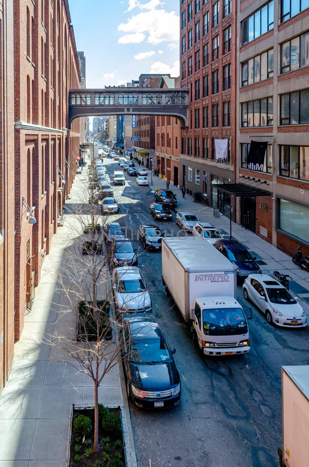 City street in Chelsea with cars and a truck passing by, aerial view from the High Line Rooftop Park, Bridge between two office Buildings, New York City during sunny winter day, vertical