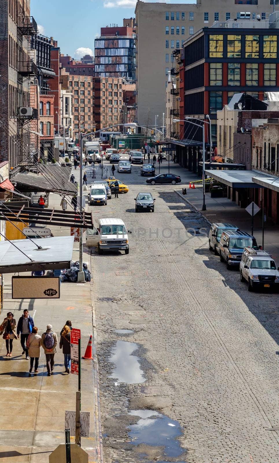 Chelsea City Street with people walking on sidewalk and traffic on the street, lots of cars parked on the street, aerial view during sunny winter day, puddle on the street, vertical
