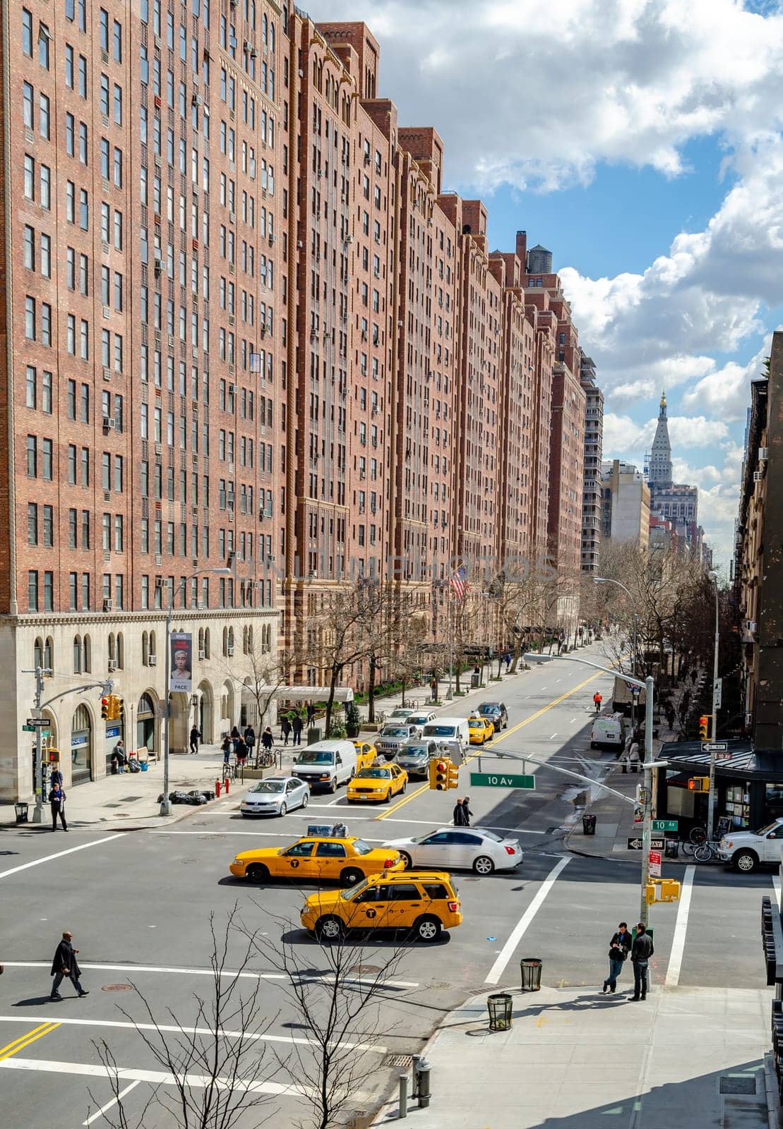 Crossroads at Chelsea, New York City with lots of yellow taxi cabs and cars passing by during sunny winter day, Brown Building facades in the background, vertical