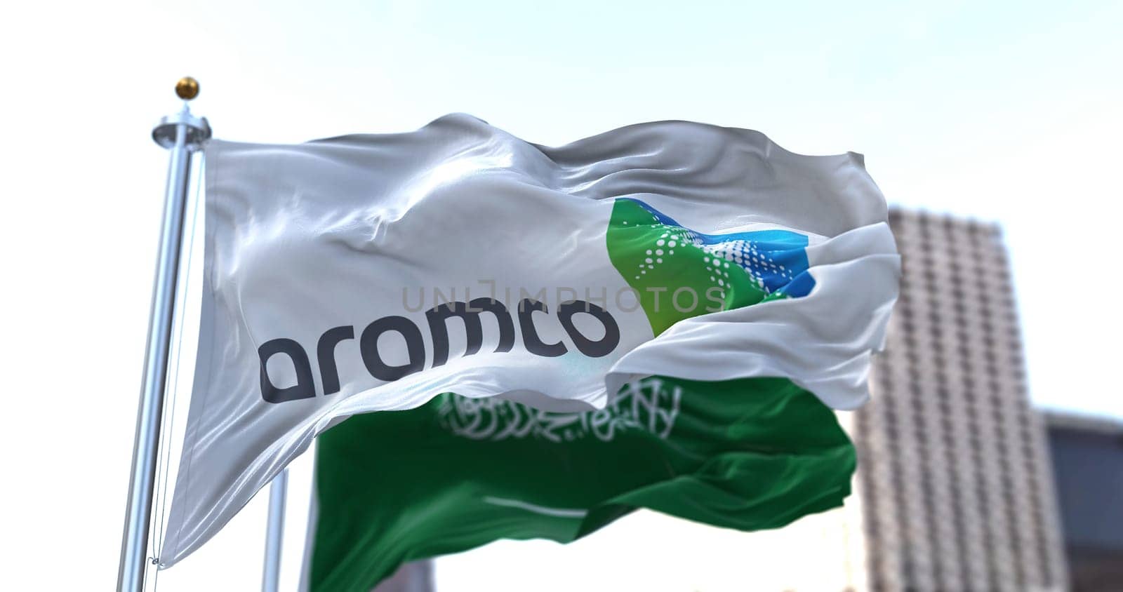 Dhahran, SA, March 2022: The flag of the Aramco oil company waving in the wind with the national flag of Saudi Arabia blurred in the background. Aramco is the Saudi national hydrocarbon company