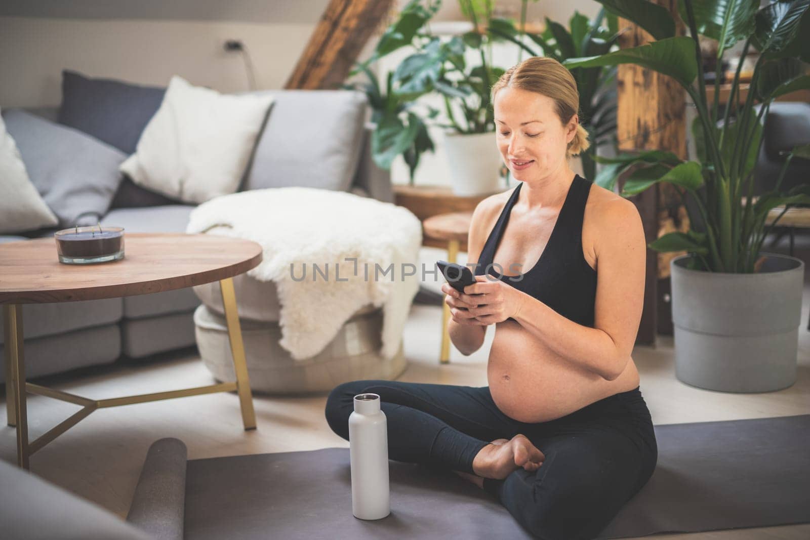 Young happy and cheerful beautiful pregnant woman chating to family and friends on mobile phone while staying fit, sporty and active on her maternity leave. Motherhood, pregnancy, yoga concept