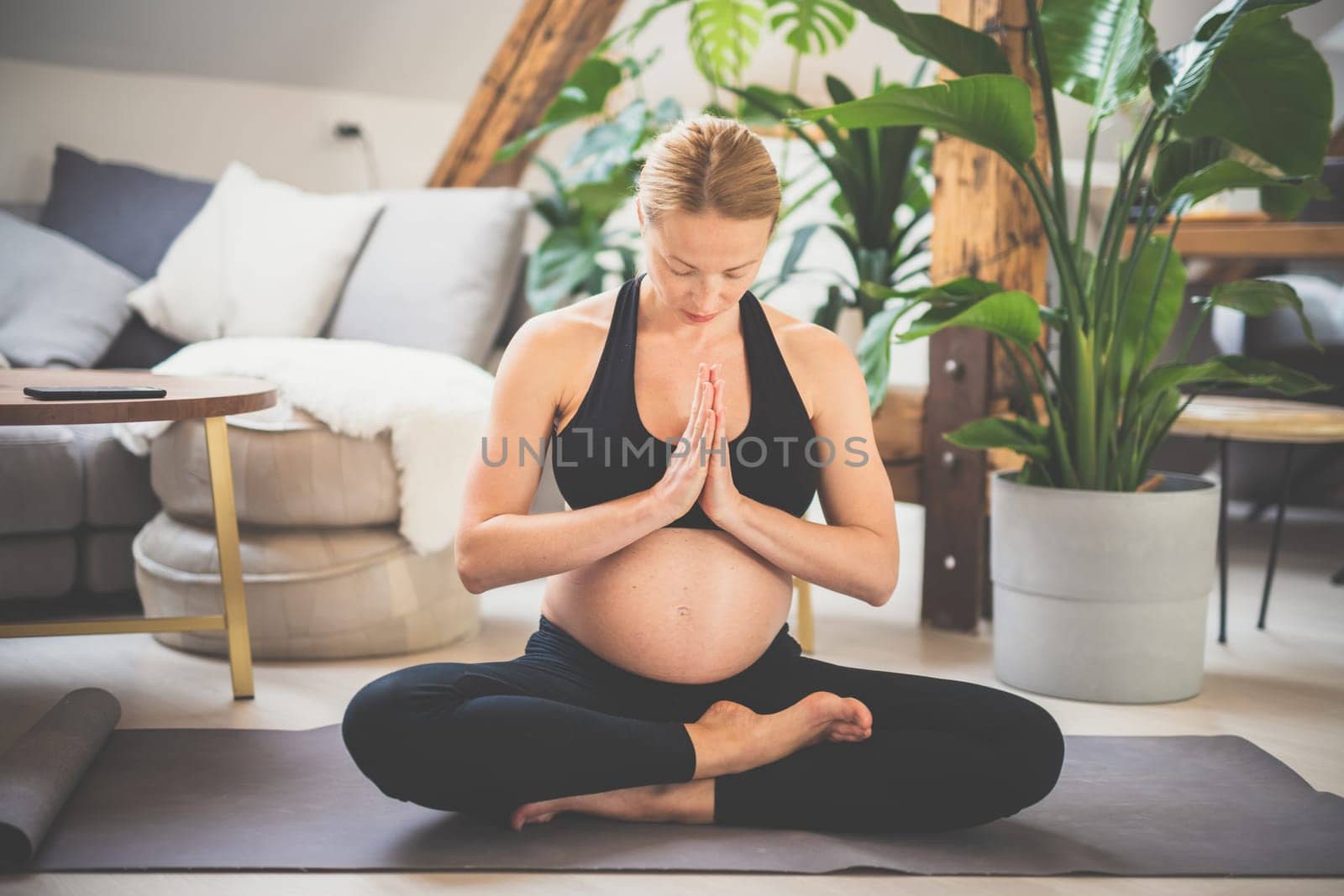 Young beautiful pregnant woman training yoga at home in her living room. Motherhood, pregnancy, healthy lifestyle and yoga concept.