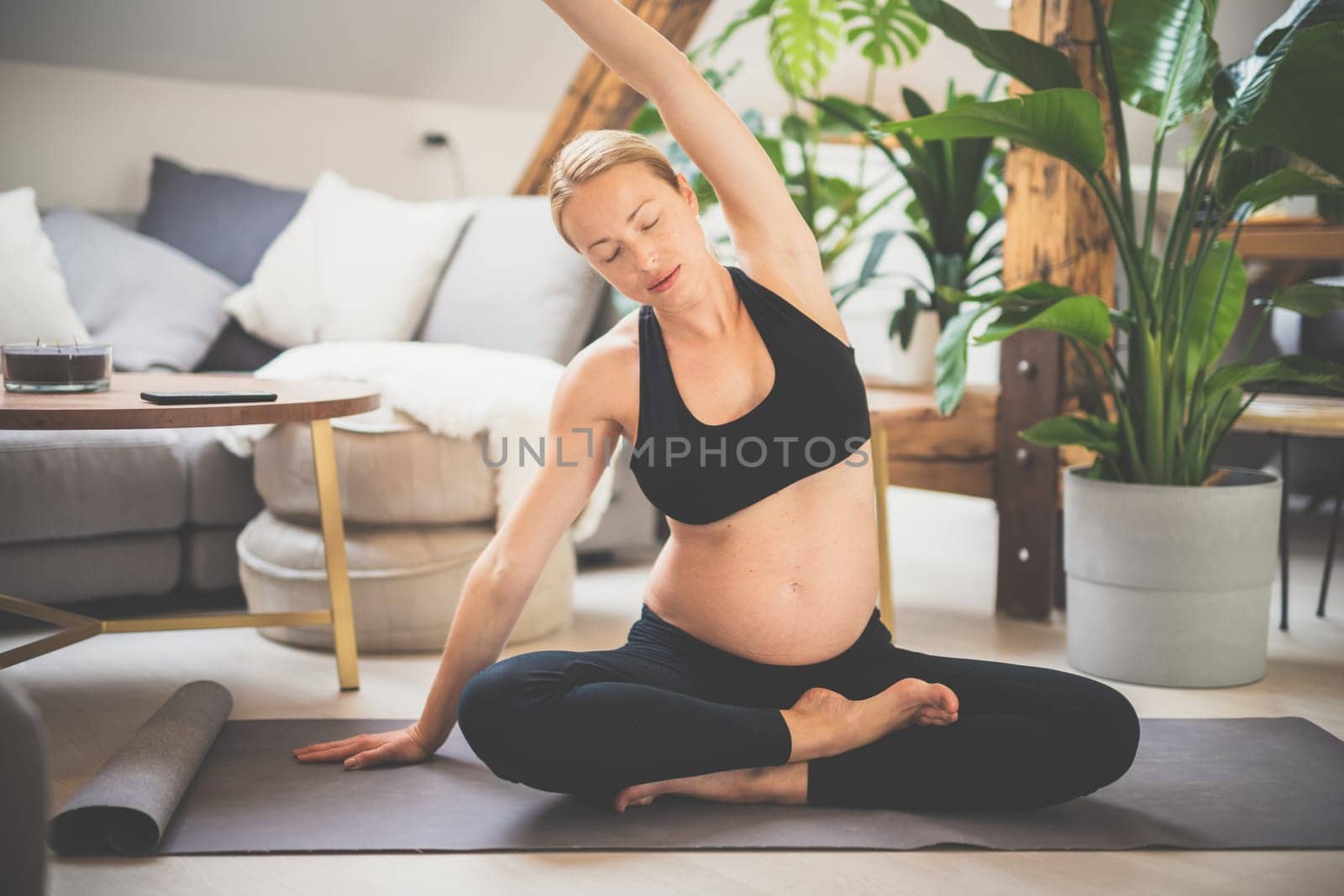 Young beautiful pregnant woman training yoga at home in her living room. Motherhood, pregnancy, healthy lifestyle and yoga concept.