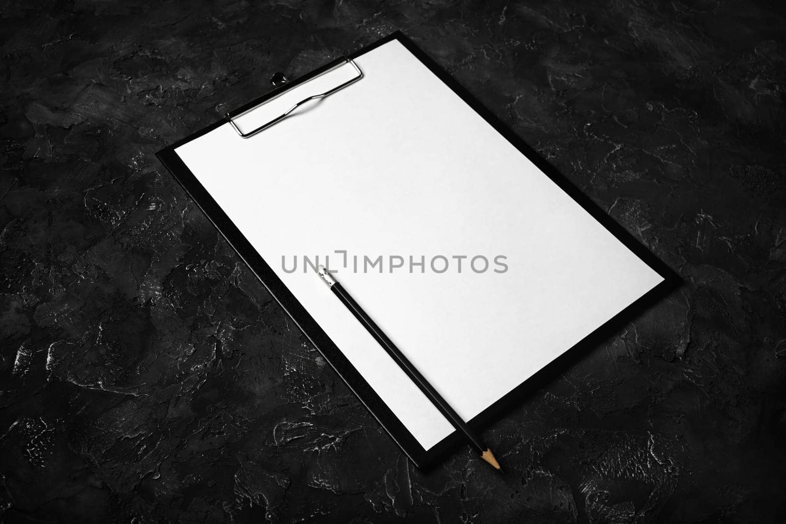 Clipboard with blank paper and pencil on black plaster background.