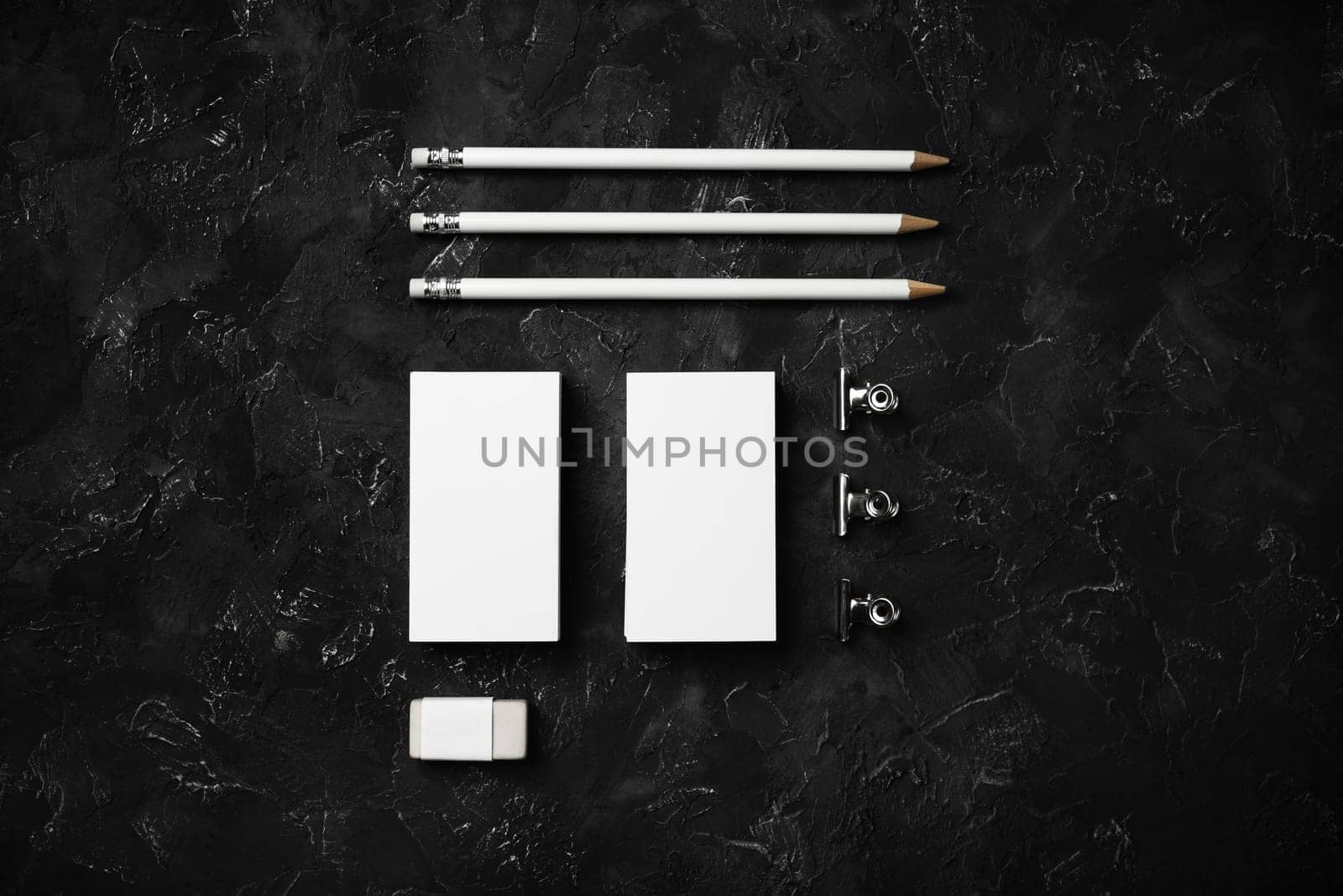 Blank business cards, pencils, eraser and clips on black plaster background. Template for graphic designers portfolios. Top view. Flat lay.