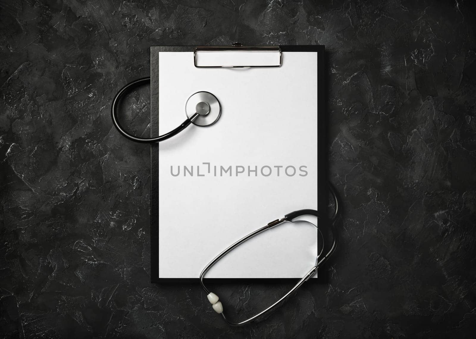 Blank medical clipboard with stethoscope on black plaster background. Copy space for text. Flat lay.
