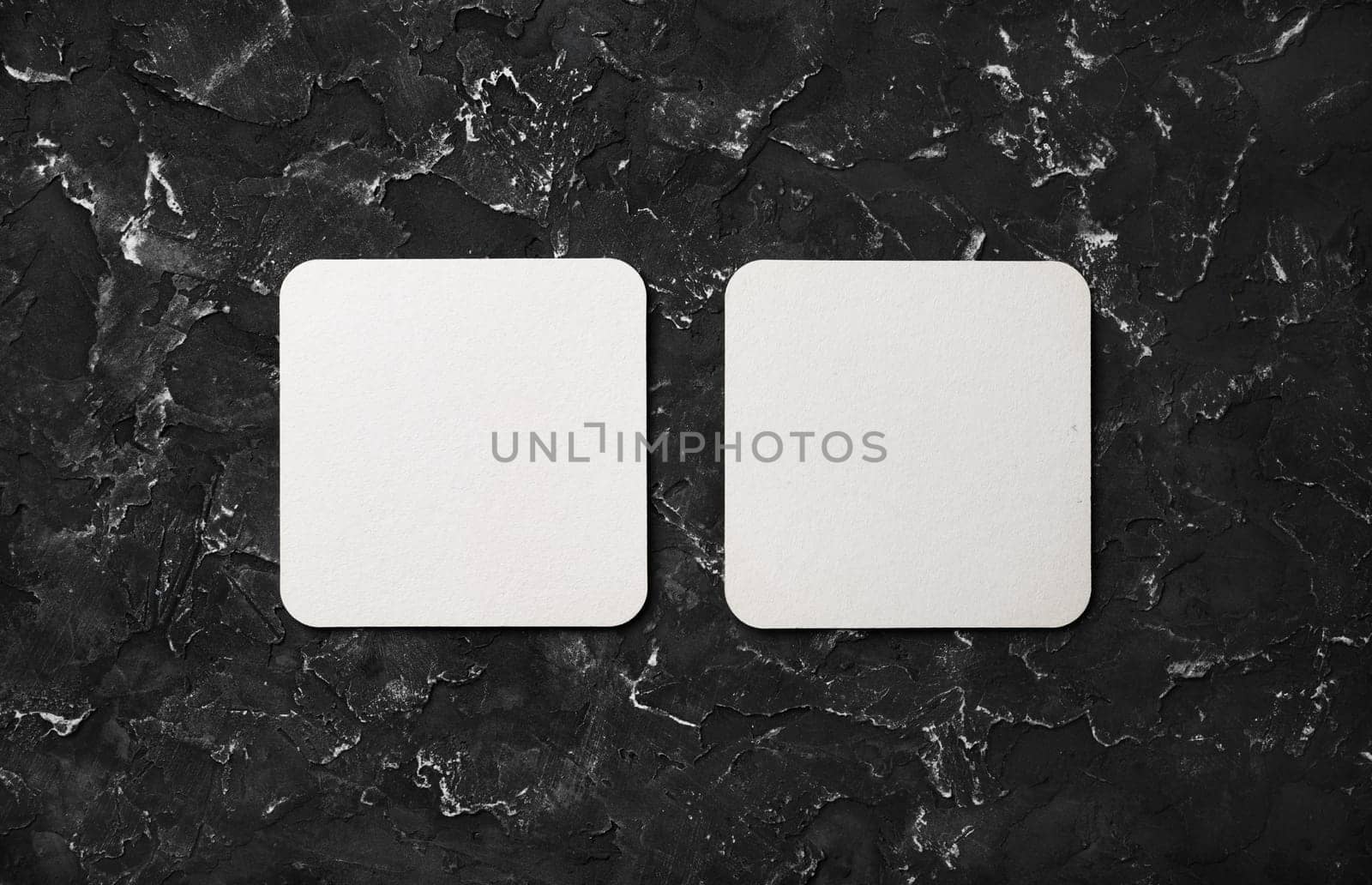Photo of two blank square beer coasters on black plaster background. Blank template for your design. Top view. Flat lay.