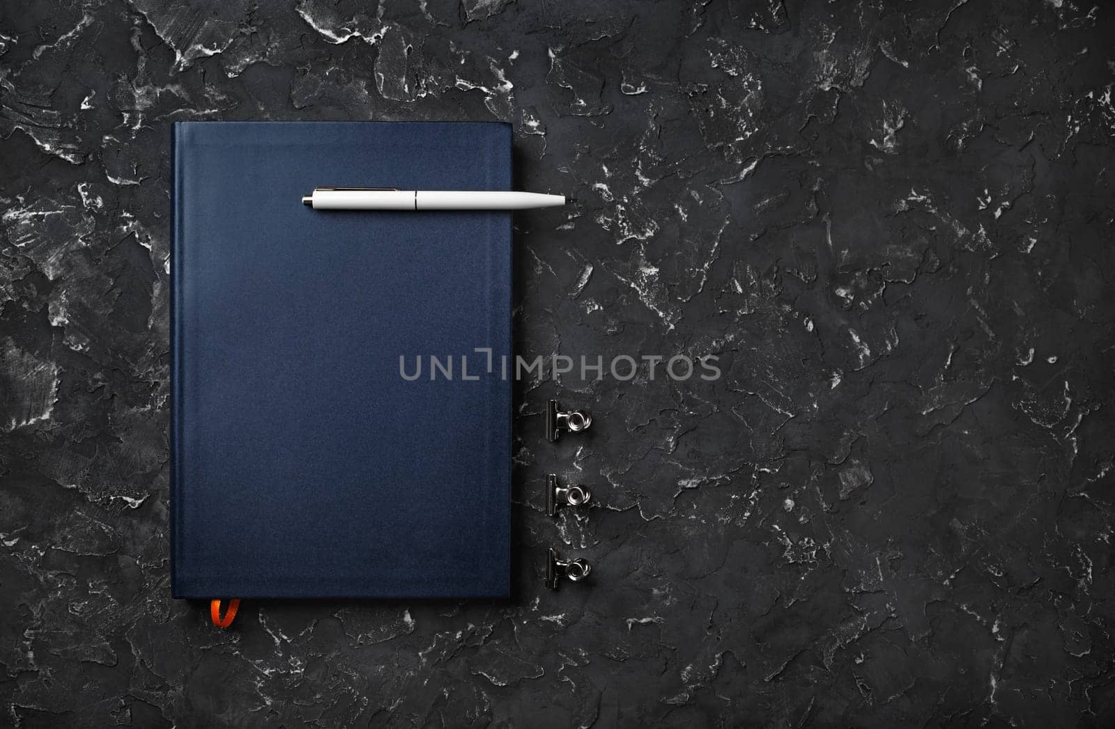 Blank blue notebook with pen on black plaster background. Copy space. Flat lay.