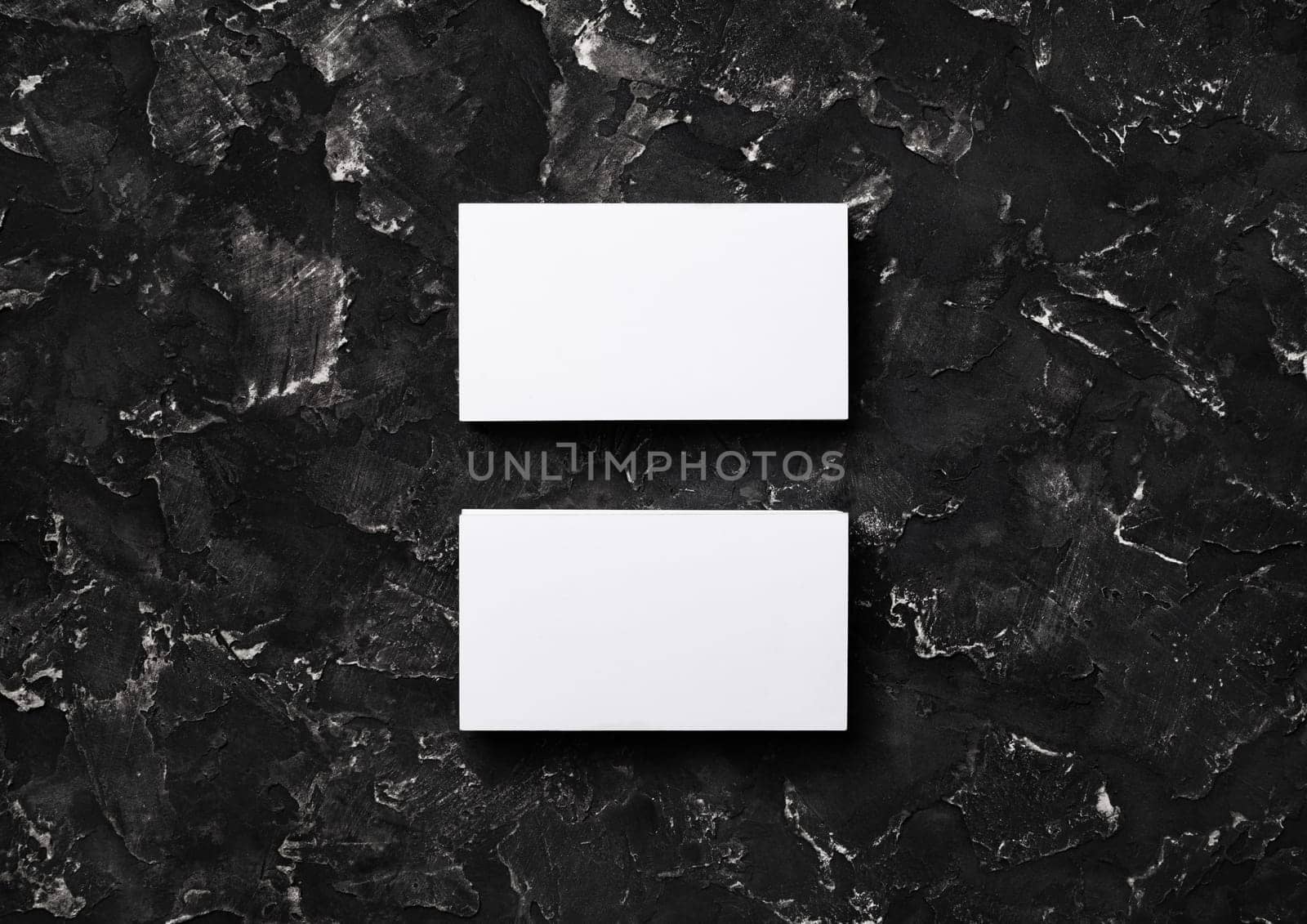 Two blank white business cards on black plaster background. Mockup for branding identity. Flat lay.