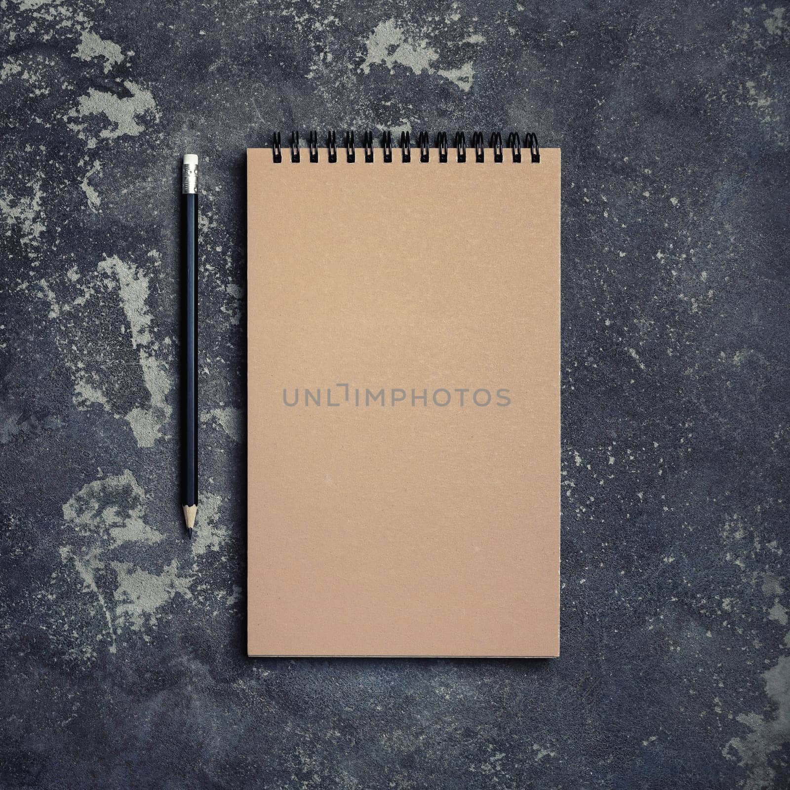 Photo of blank kraft notebook and pencil on concrete background. Top view. Flat lay.