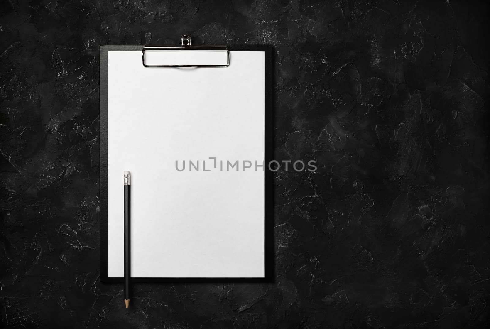 Blank clipboard and pencil on black plaster background. Copy space for text. Top view. Flat lay.