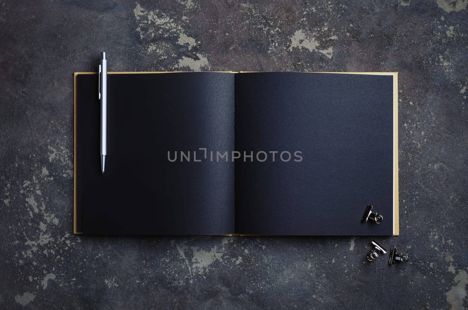 Blank black brochure, pen and clips on concrete background. Template for placing your design. Top view. Flat lay.