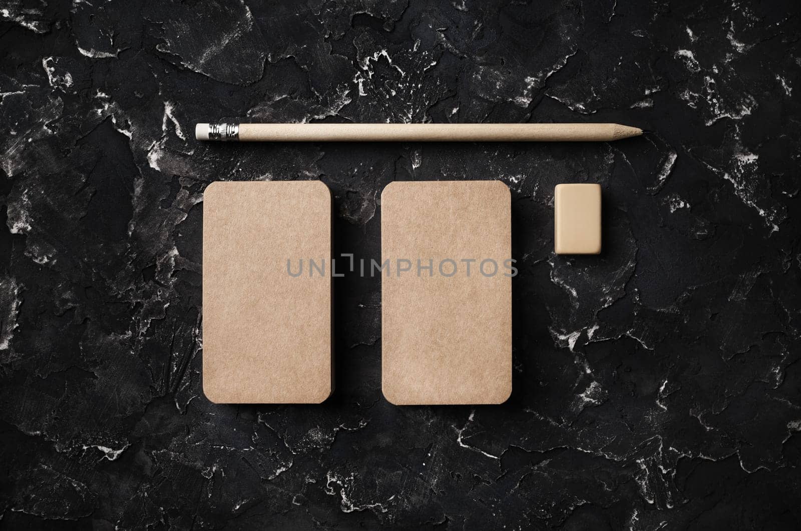 Photo of blank kraft business cards, pencil and eraser on black plaster background. Top view. Flat lay.