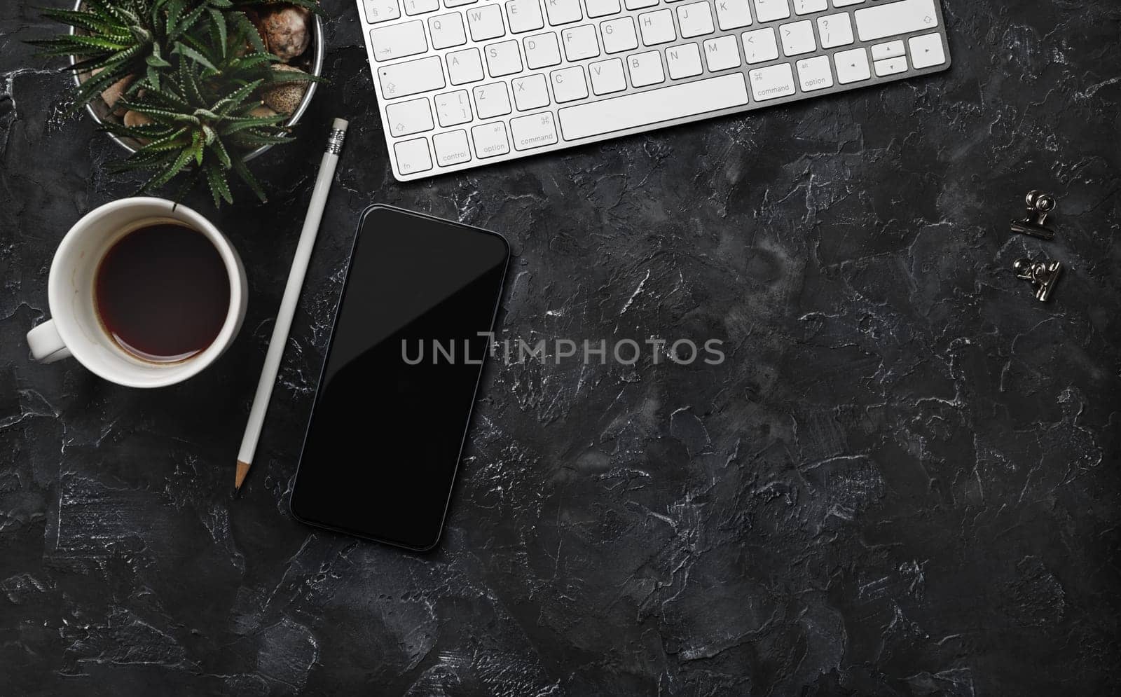 Top view of work space with keyboard, smartphone, coffee cup, succulent plant and pencil on black plaster background. Flat lay.