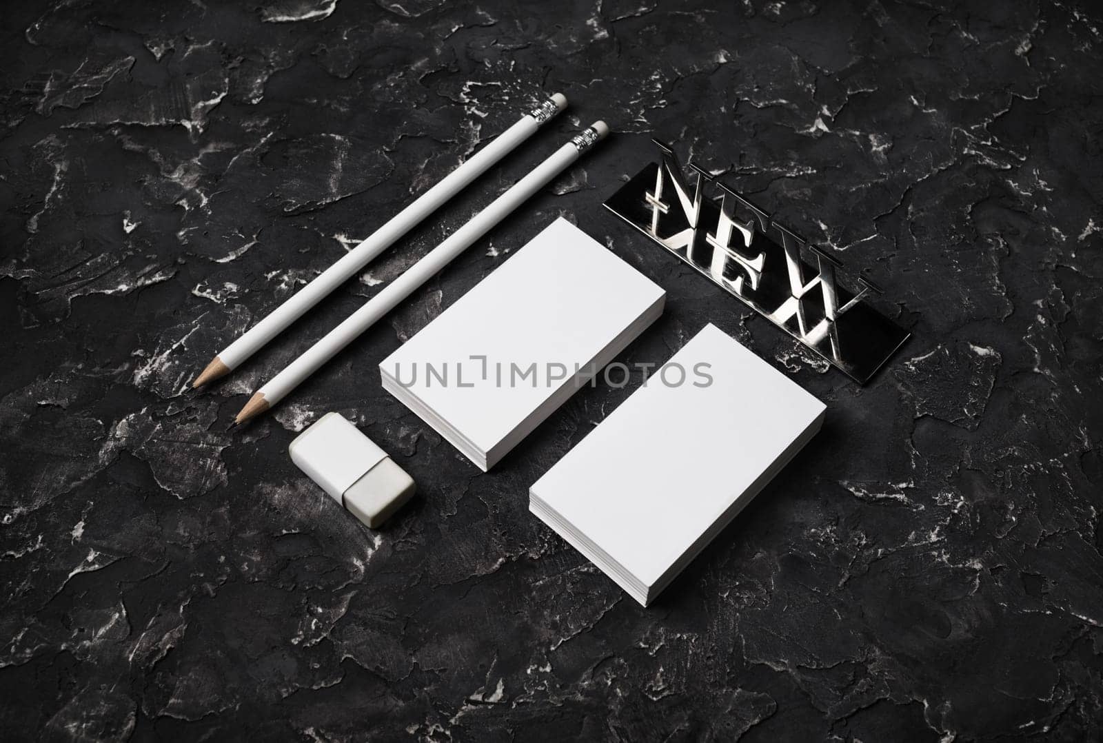 Blank stationery template. Blank business cards, pencils, eraser and new metal plate on black plaster background.