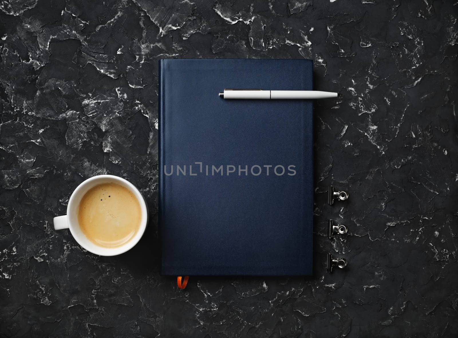 Blank notepad, pen, coffee cup and clips on black plaster background. Top view. Flat lay.