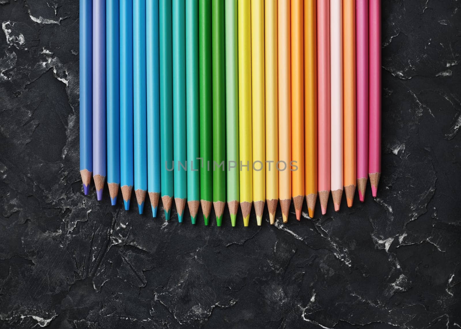Collection of rainbow colored pencils on black plaster background. Top view. Flat lay.