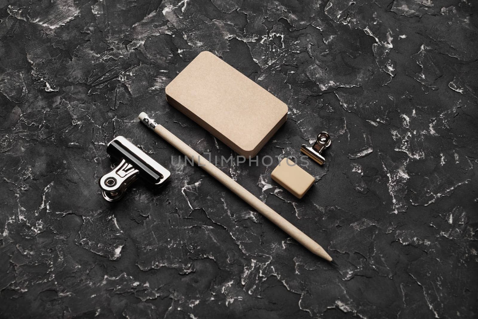 Photo of blank vintage business cards, pencil, eraser and clips on black plaster background. Blank kraft stationery.