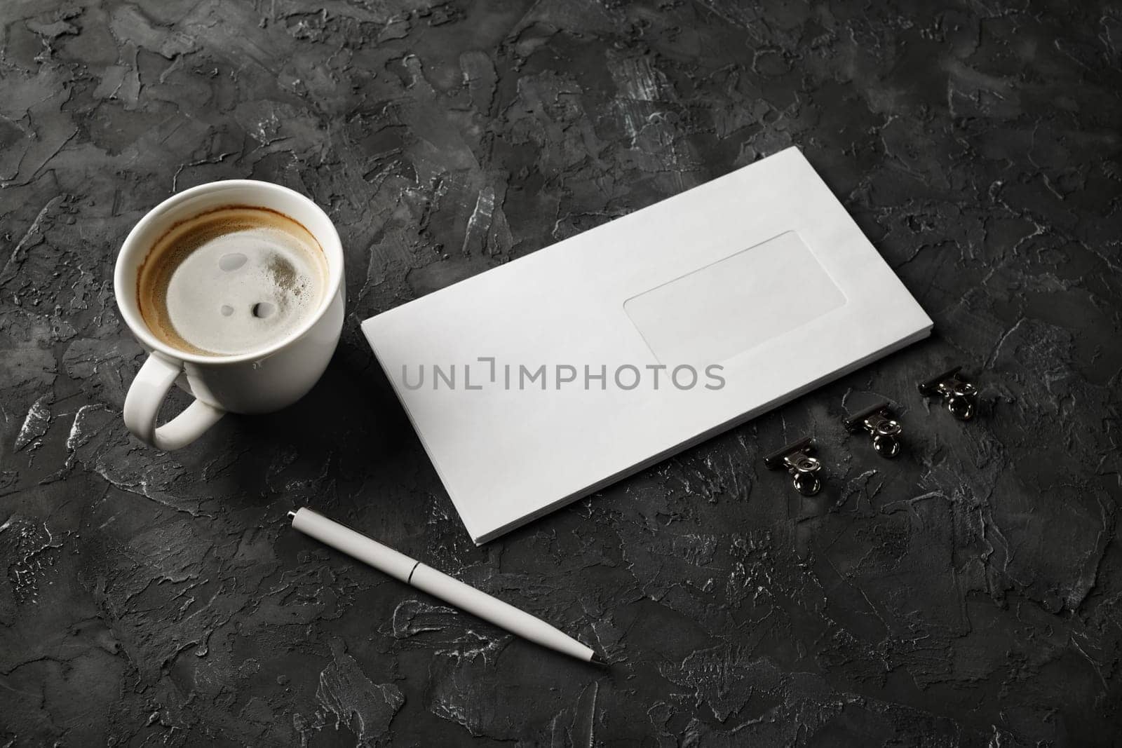 Blank envelope, coffee cup, pen and clips on black plaster background. Branding mock up.