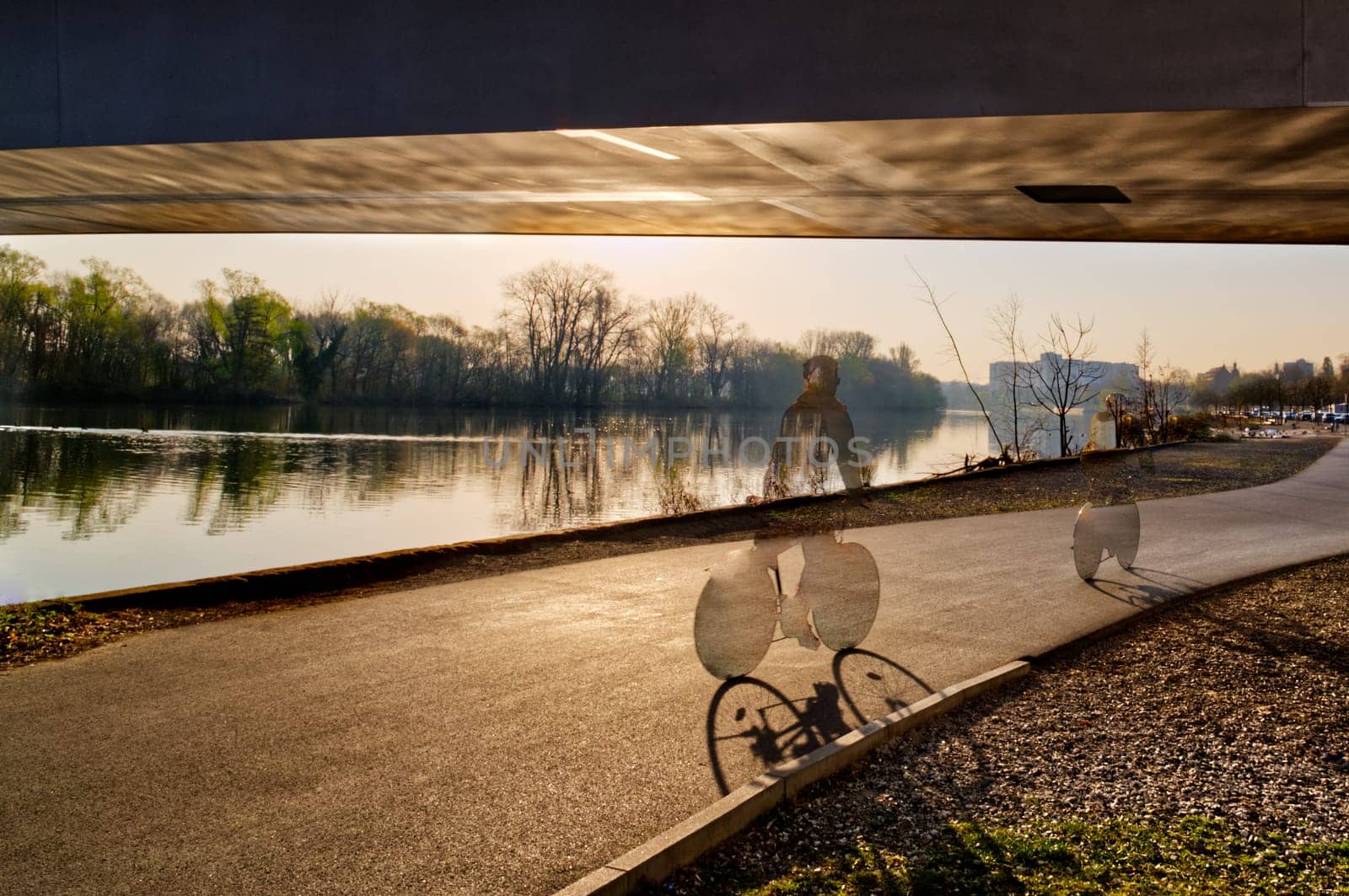 bike / biking person (translucent) on a riverside underneath a bridge , digitally processed
