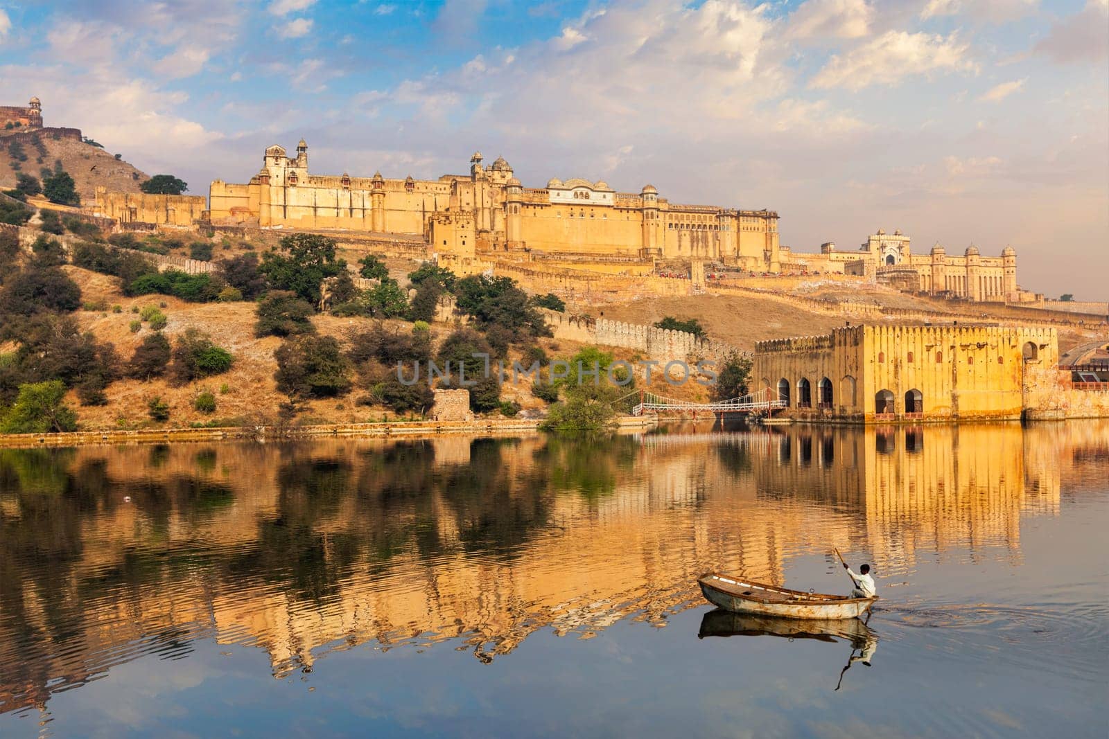 Famous tourist destination Amer (Amber) fort and Maota lake with man in boat in the morning. Jaipur, Rajasthan, India