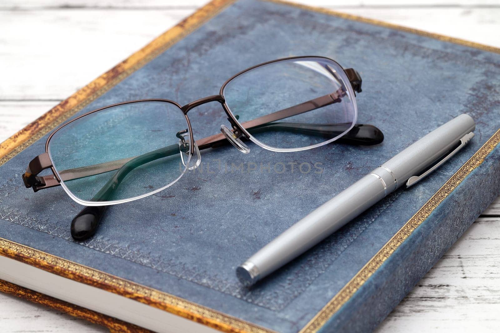 Stylish eyesight glasses and diary book on white wooden table