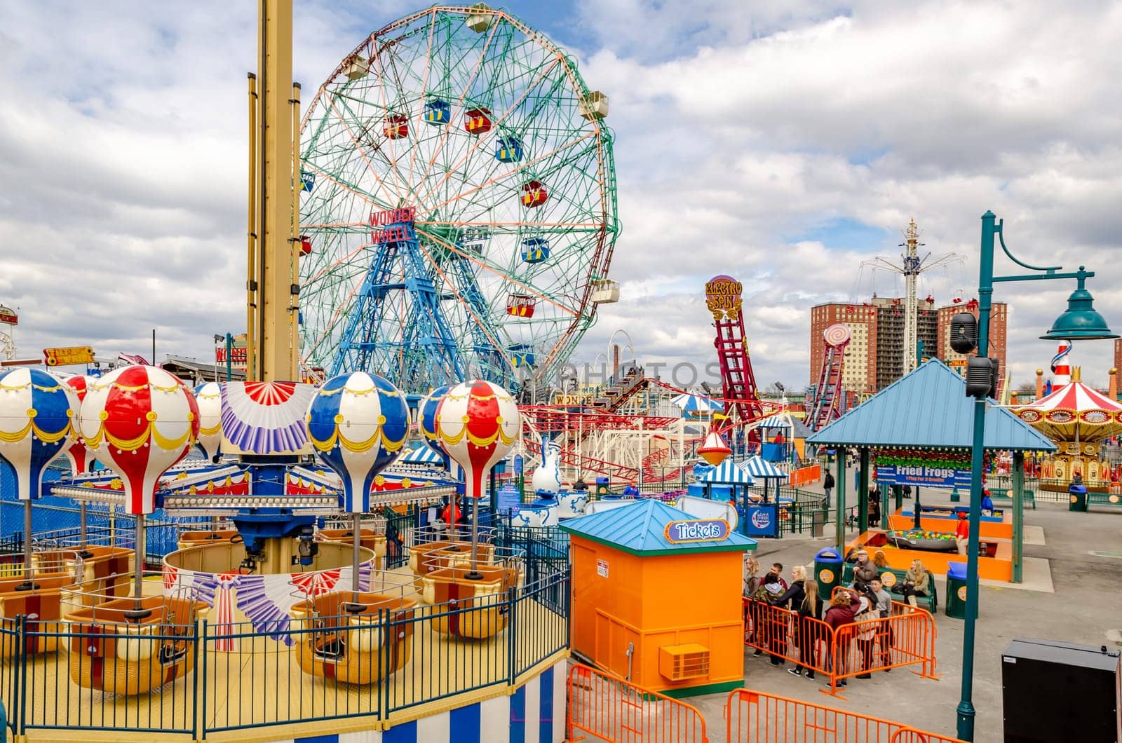 Luna Park Amusement Park at Coney island, Brooklyn, different rides and People waiting in Line during Jewish National Day, New York City, winter day with cloudy sky, Residential Building in the background, horizontal