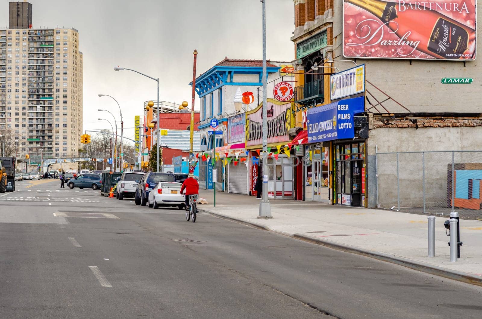 Stores and Restaurants at City Street in Coney island, Brooklyn, New York City during winter day with cloudy sky, Cars parked next to the street in front of the stores, Residential Building in the Background, horizontal