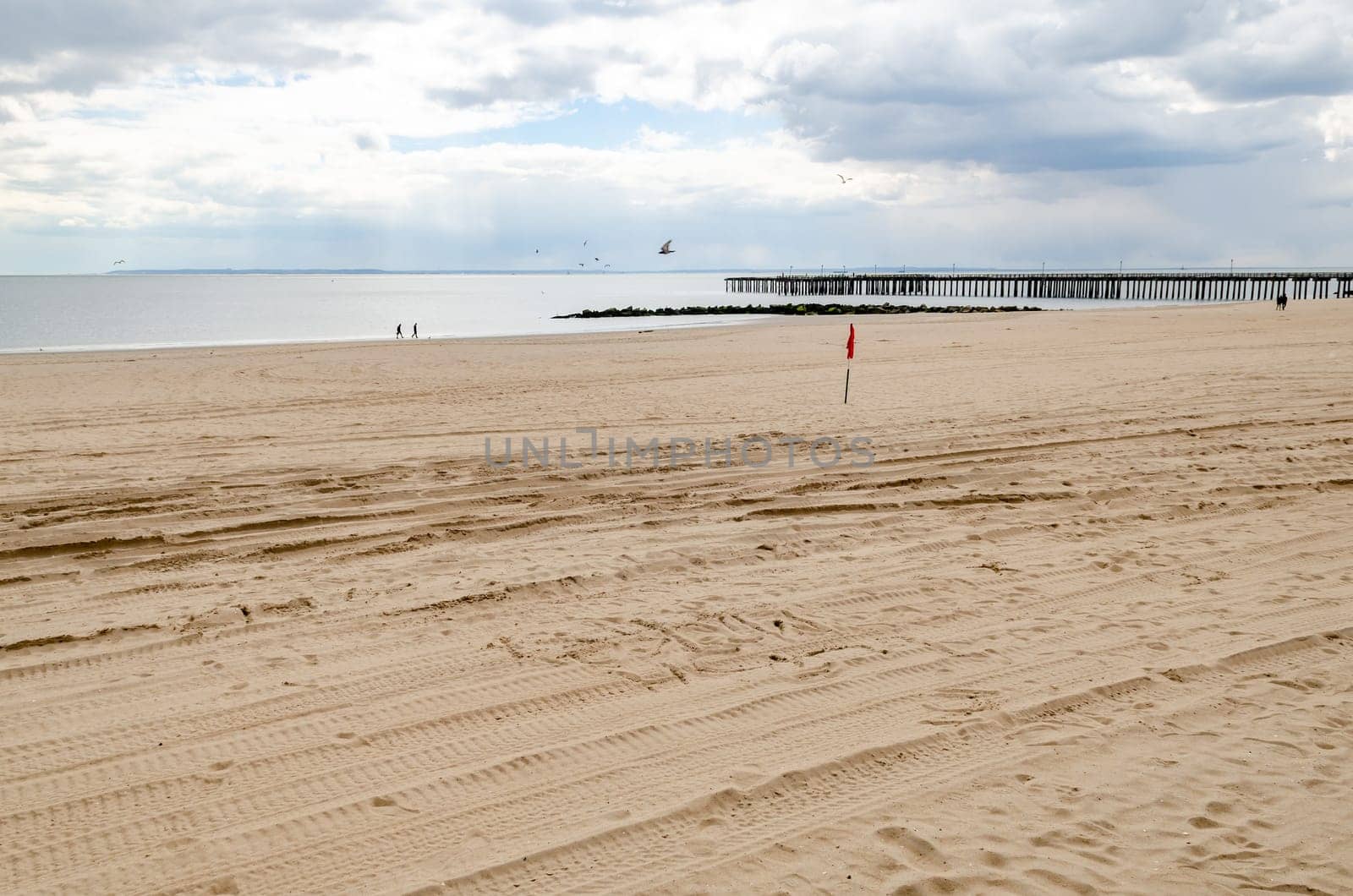 Beach at Coney island, Brooklyn with Ocean and Pat Auletta Steeplechase Pier, New York City during winter day with cloudy sky, almost no People at the Beach, horizontal
