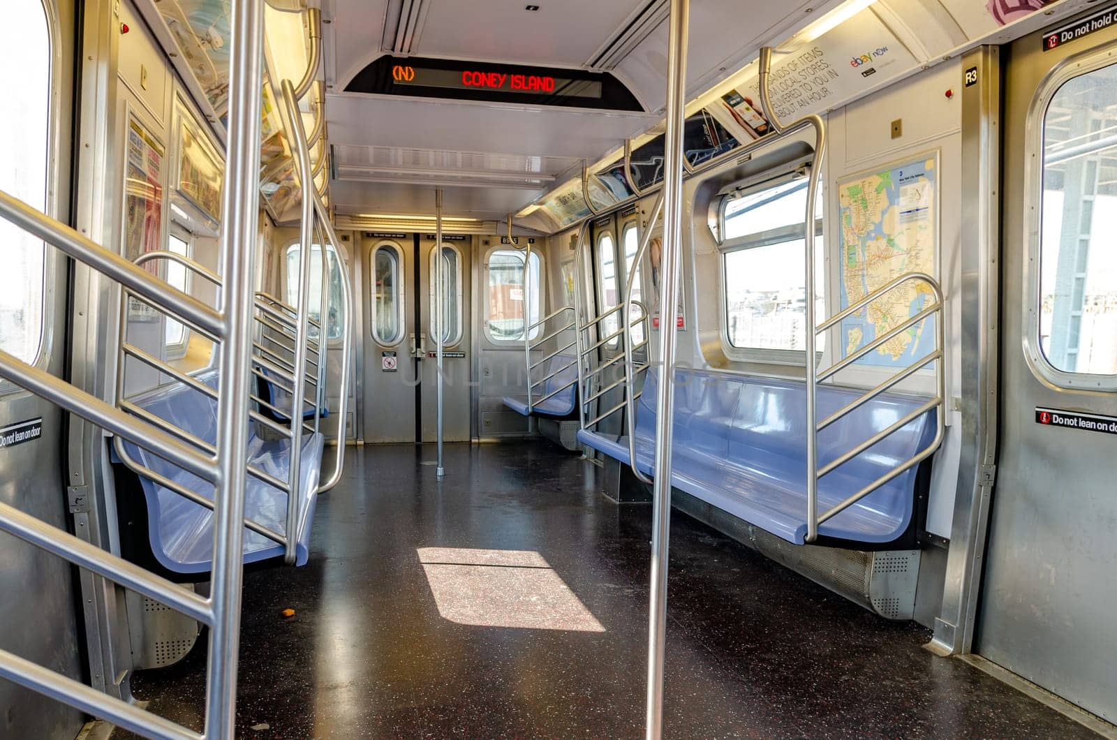 Subway New York City indoors, empty, destination to Coney island, Brooklyn, red lettering on screen at the roof of the train, indoors with blue benches, driving above ground during sunny day, horizontal