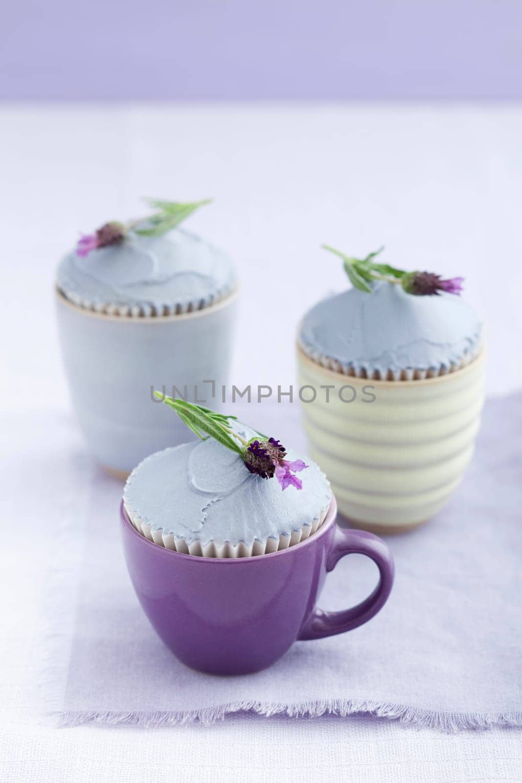 Three cupcakes with lavender buttercream and lavender flowers on a purple tablecloth