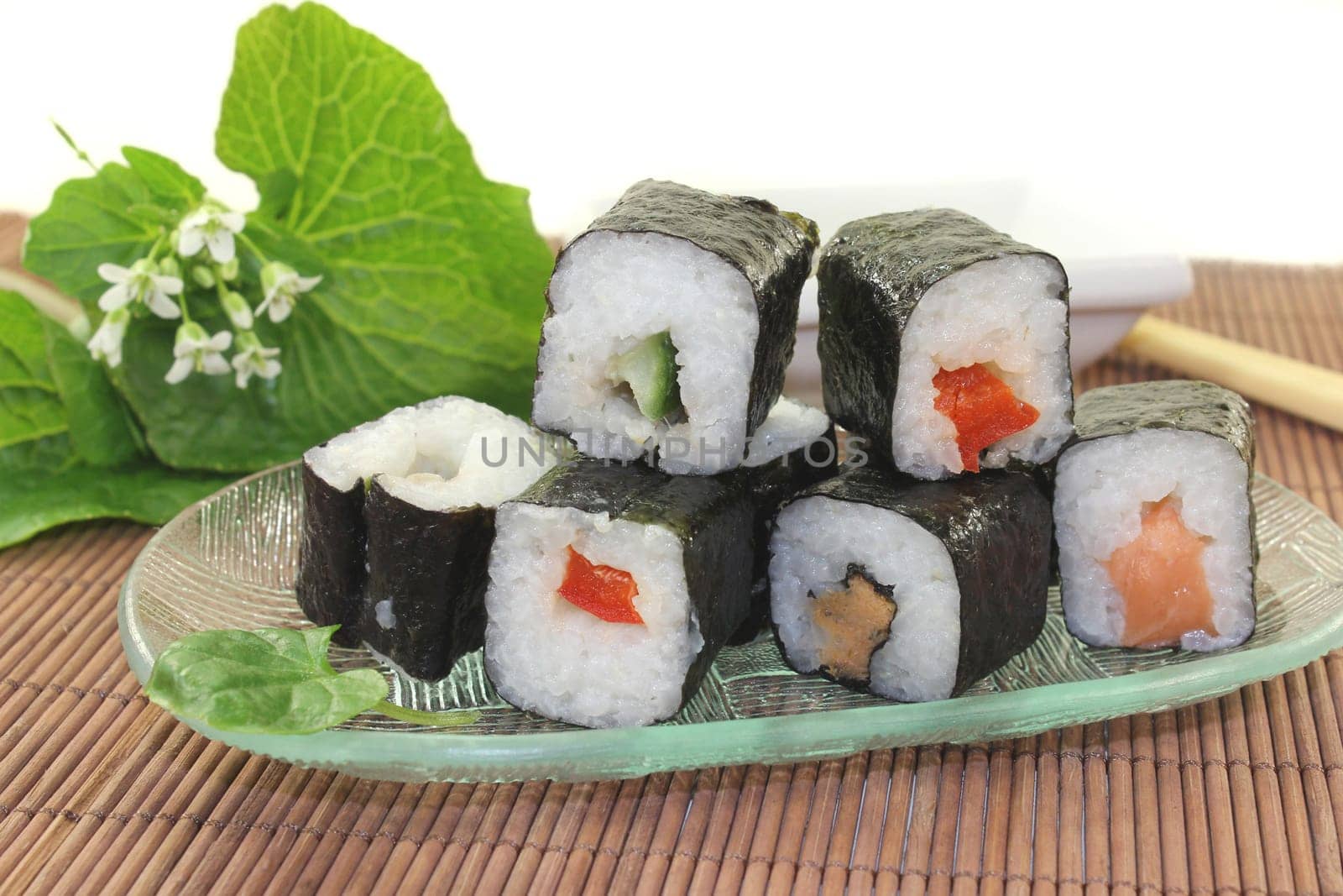 a glass bowl with sushi and fresh wasabi leaves